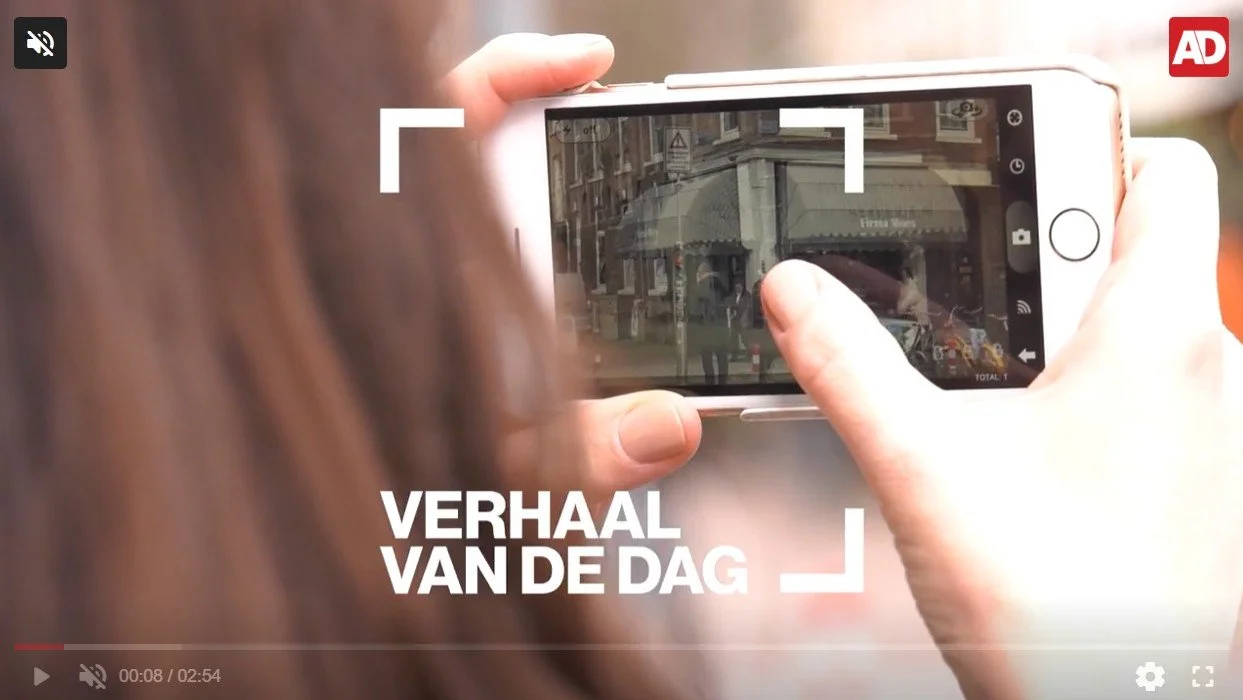 A person taking a photo of a building on a city street with a smartphone. Text on the image reads "Verhaal van de dag" and the Algemeen Dagblad logo in the top right corner.