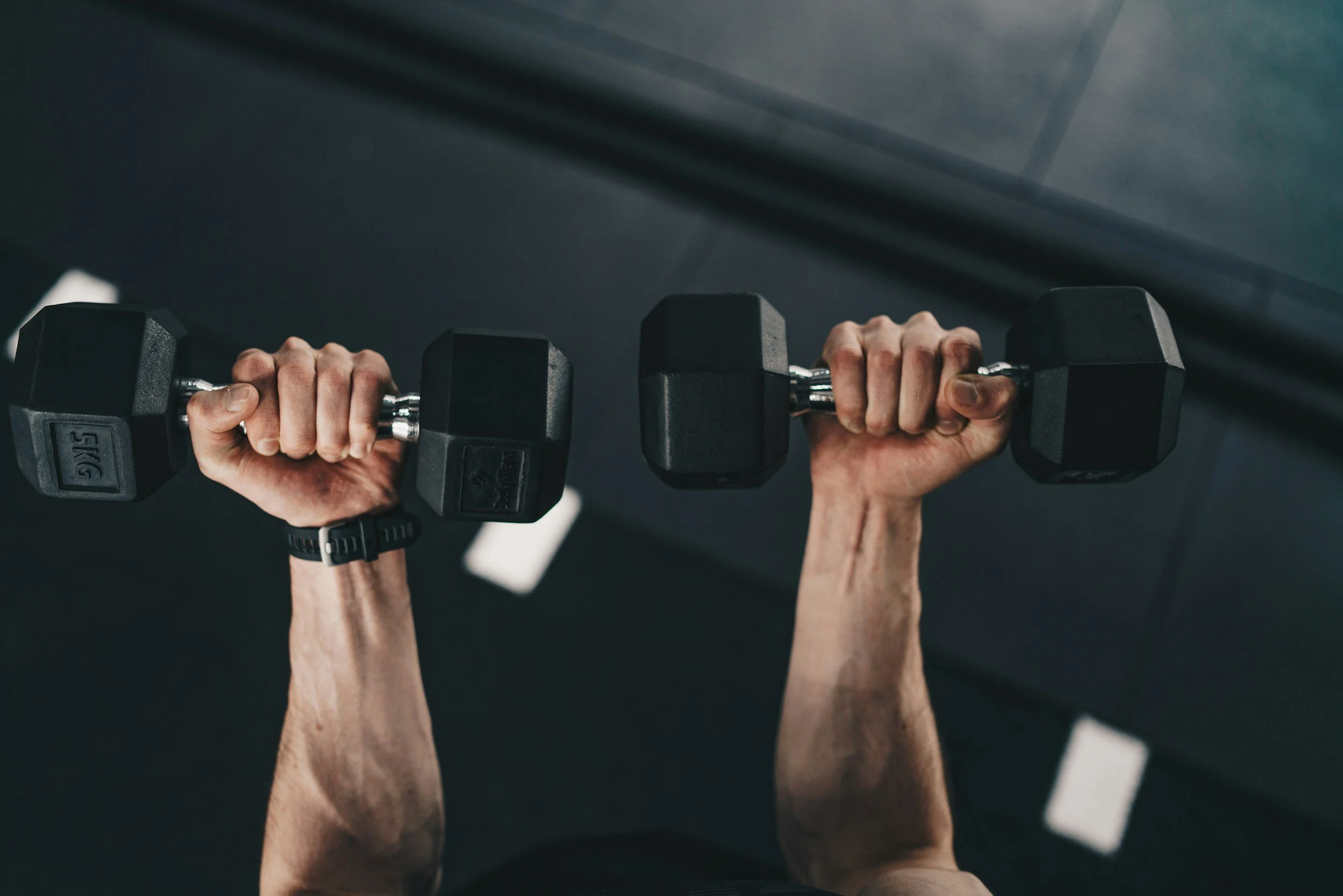 Person lifting black dumbbells during workout at gym.