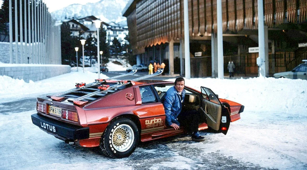 James Bond stepping out of a red vintage Lotus Esprit sports car in a snowy mountainous area.