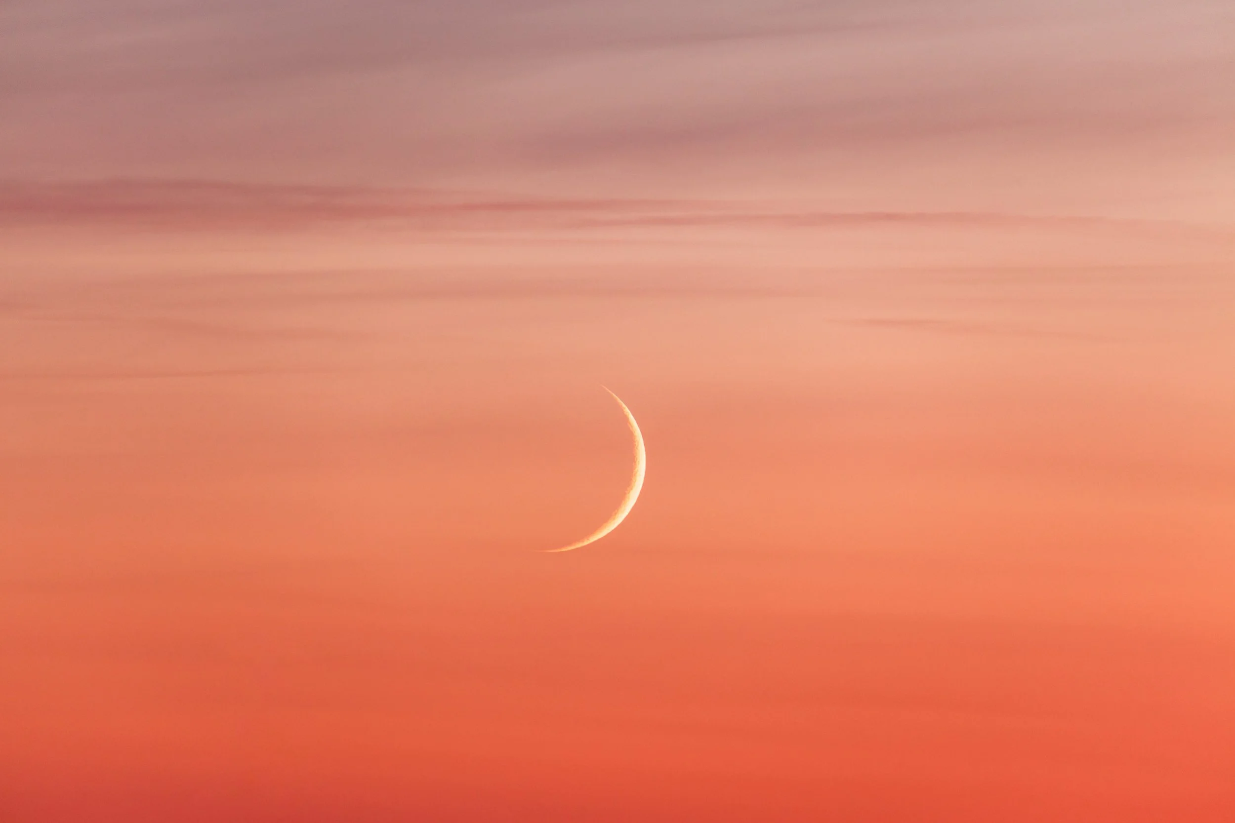 A crescent moon in a colorful sunset sky with shades of pink, orange, and purple.