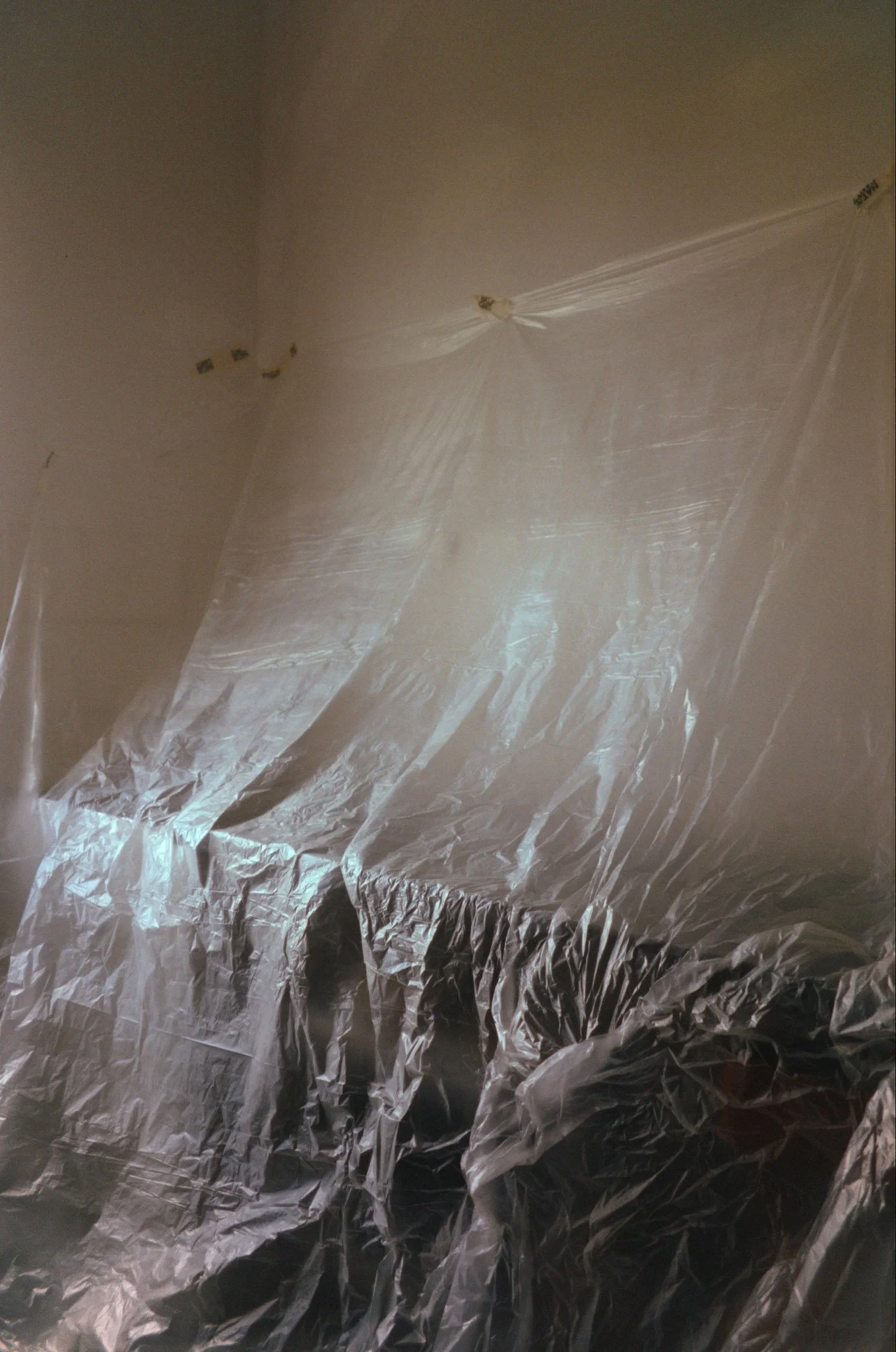 A room covered with clear plastic sheeting over furniture, likely for painting or protection.
