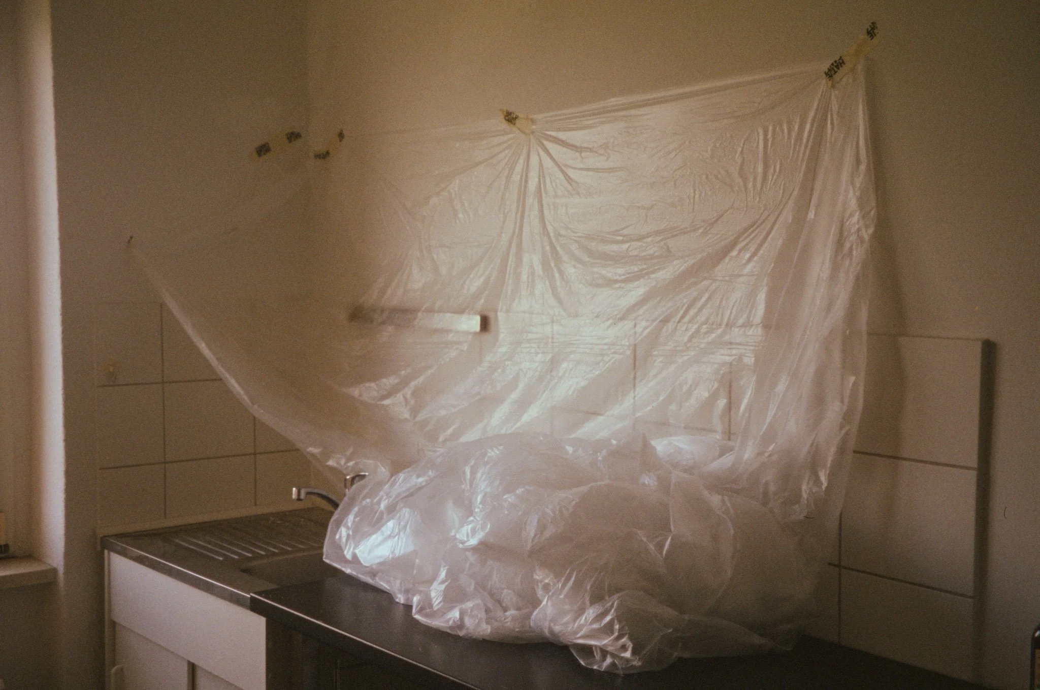 Clear plastic sheet hanging above a kitchen sink, partially covering a pile of plastic bags or cling wrap on a countertop.