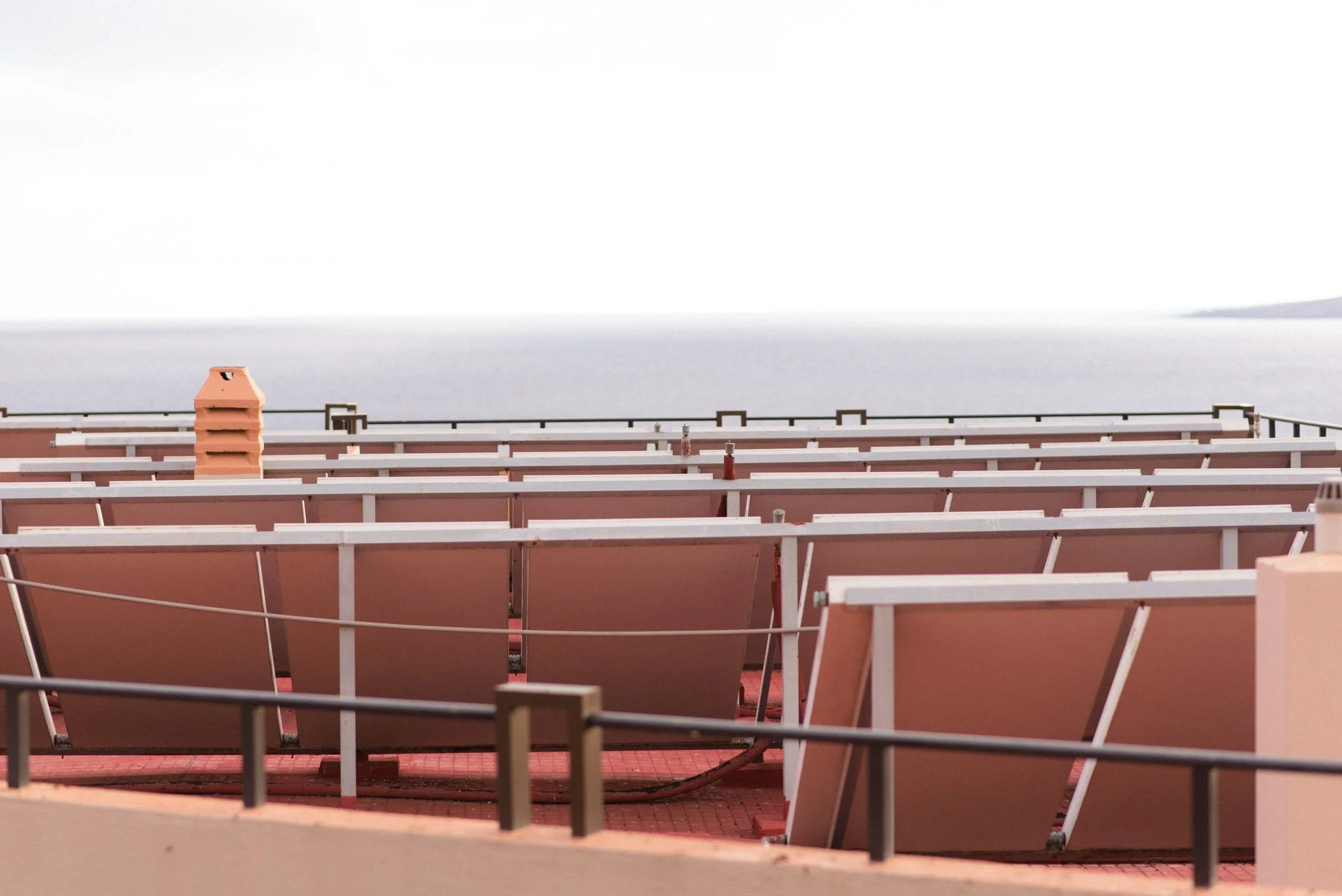 View of rooftop solar panels installed on a pink building with a chimney and a flat gray rooftop in the background.