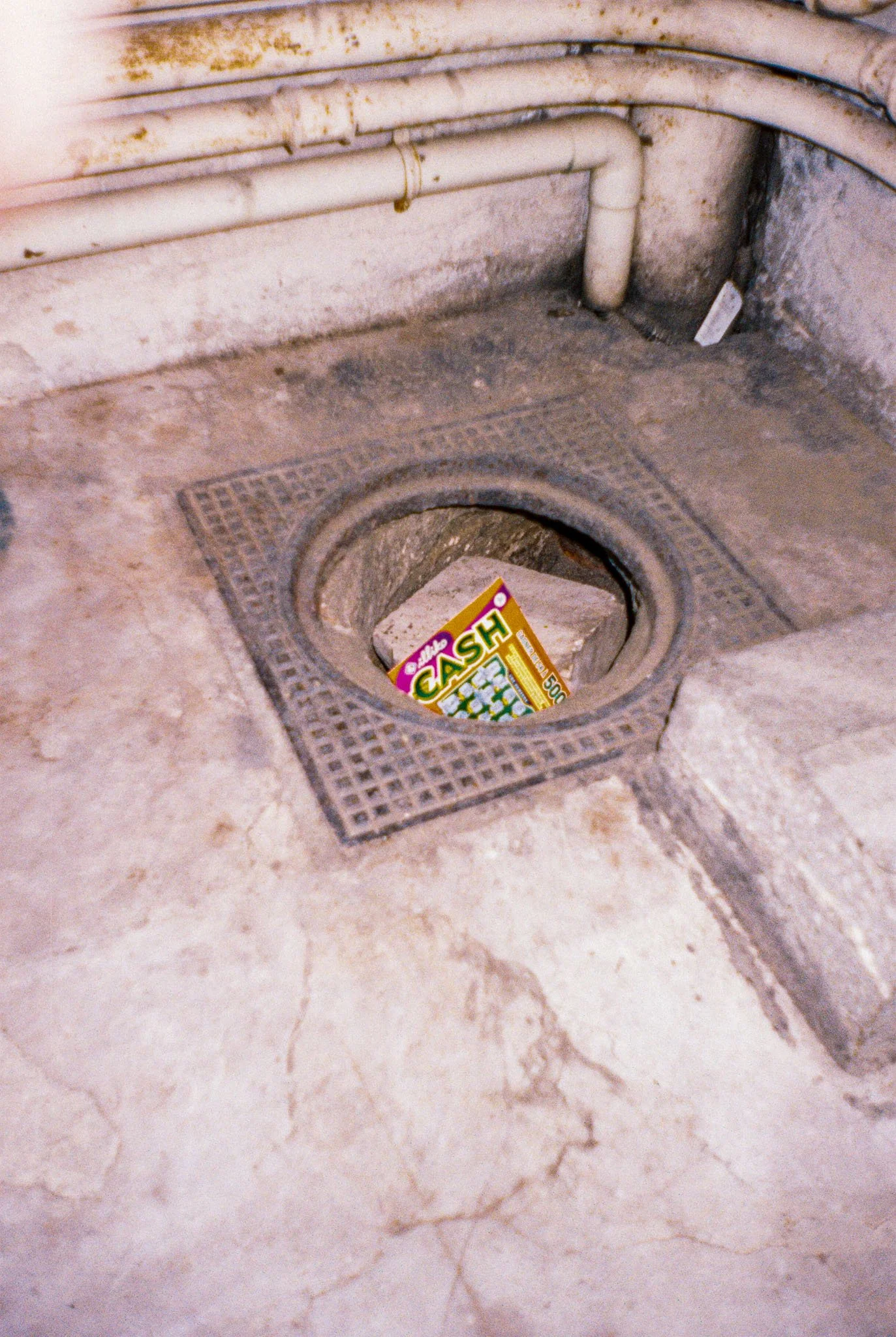 A drain in the floor with a cardboard box labeled 'Cash' and a trash bag inside.