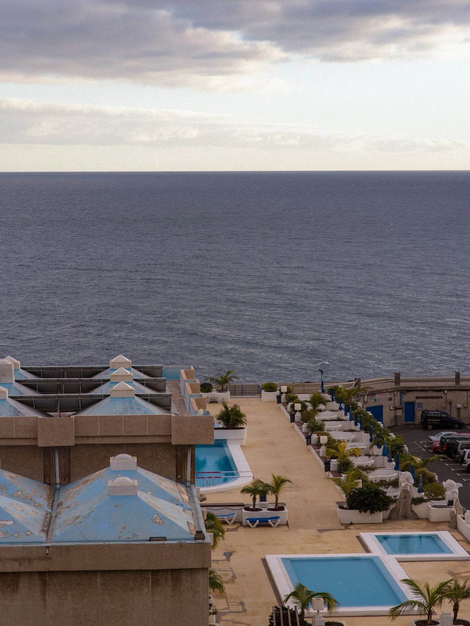 A view of a rooftop pool area overlooking the ocean with a cloudy sky.