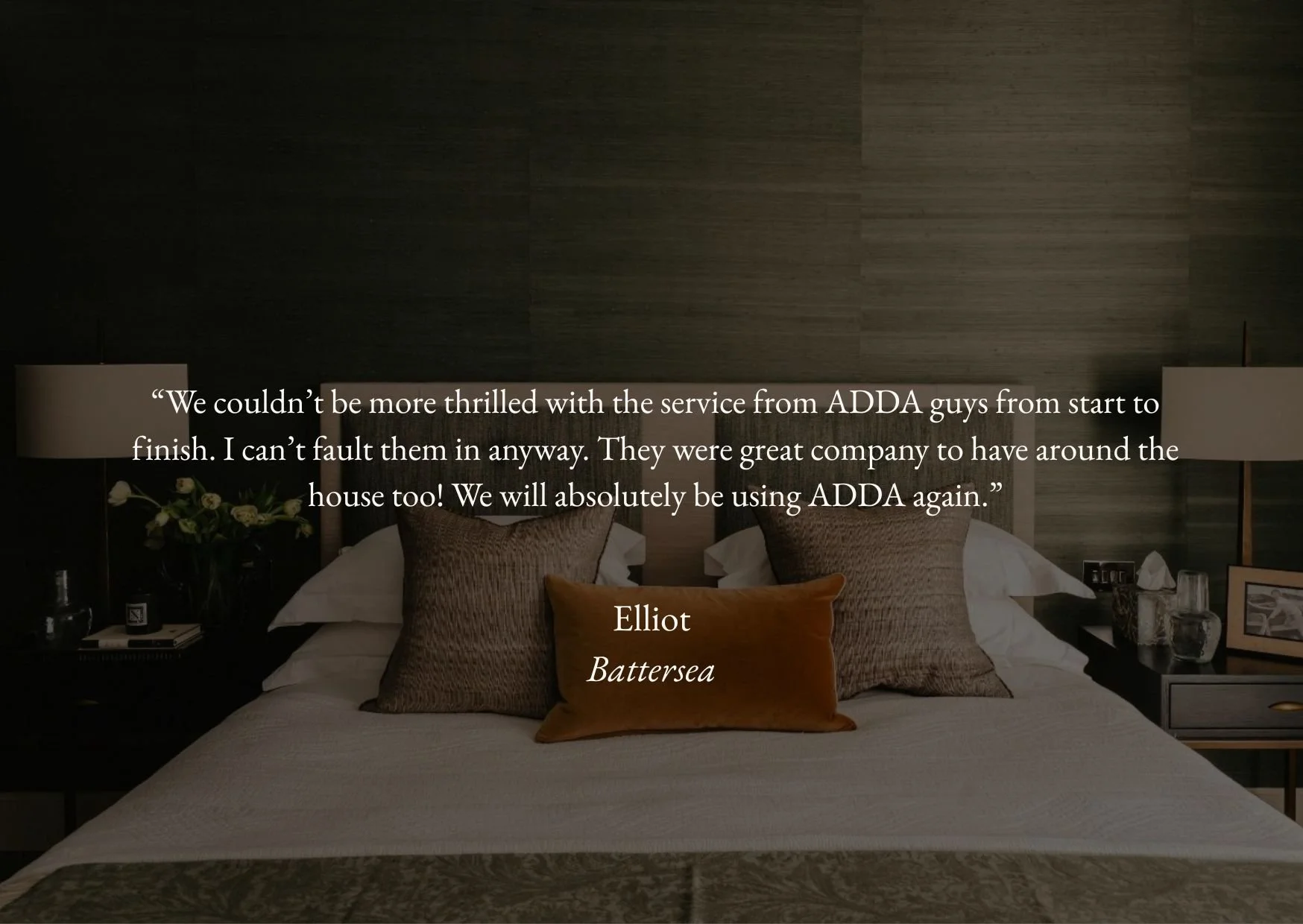 A neatly made bed with a brown velvet pillow in a modern bedroom with dark-paneled wall and side tables with lamps and decorative items.