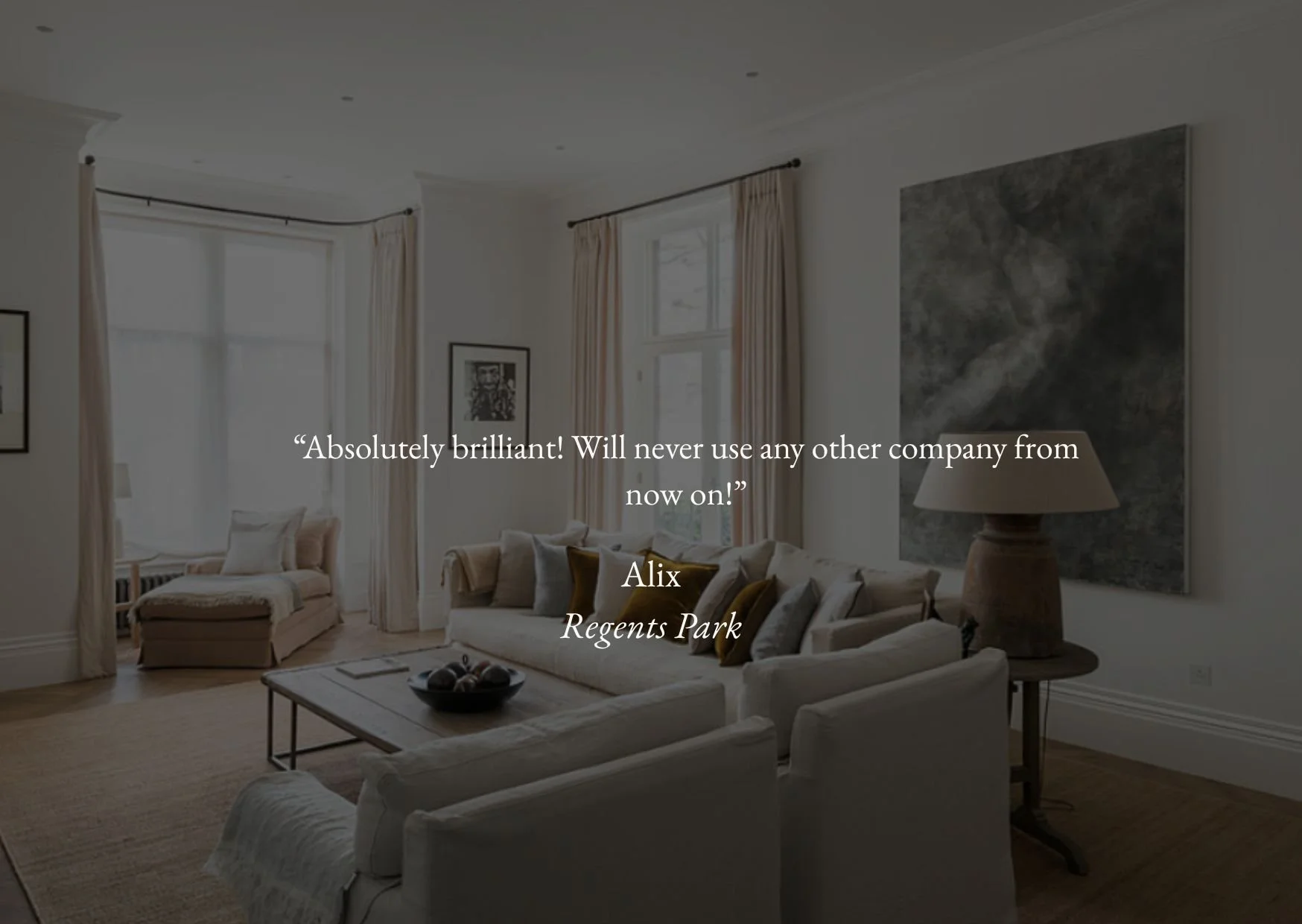 Elegant living room with white sofas, a coffee table, large windows with cream curtains, and artwork on the walls.