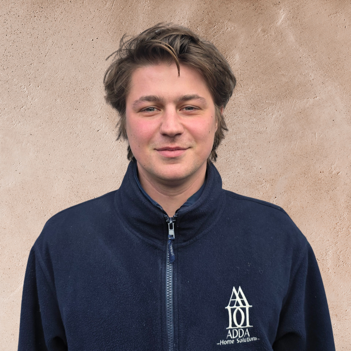 Close-up of a smiling woman with black hair, wearing a blue top, surrounded by green plants.