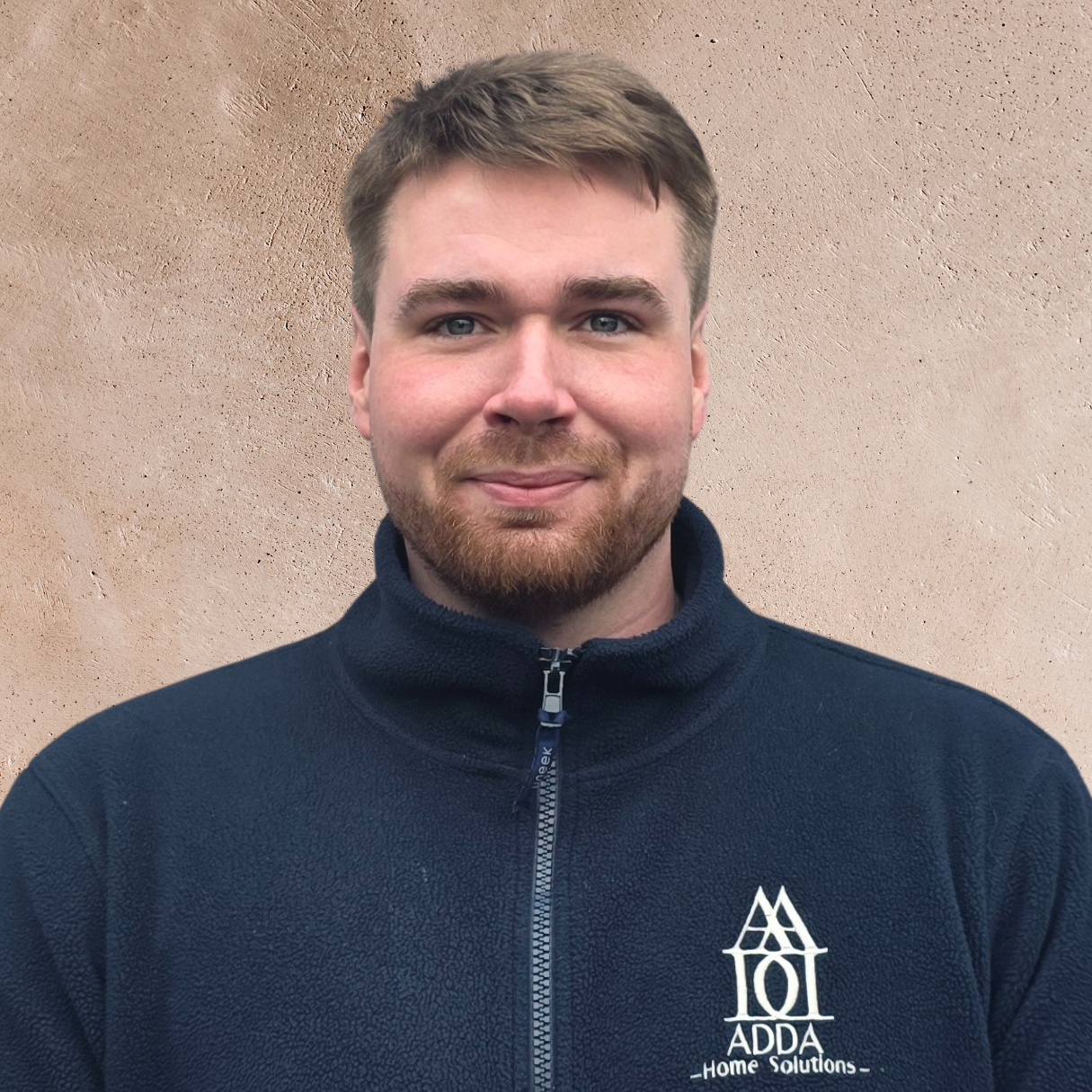 Smiling young woman with curly hair, wearing glasses, earrings, and layered necklaces, indoors with blurred background.