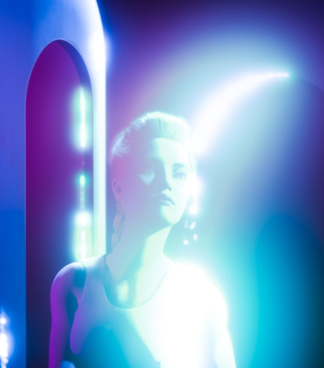 Artistly AI, Lyra Drake illuminated by vibrant blue and purple neon lights, standing in front of a futuristic mirror with glowing lights.