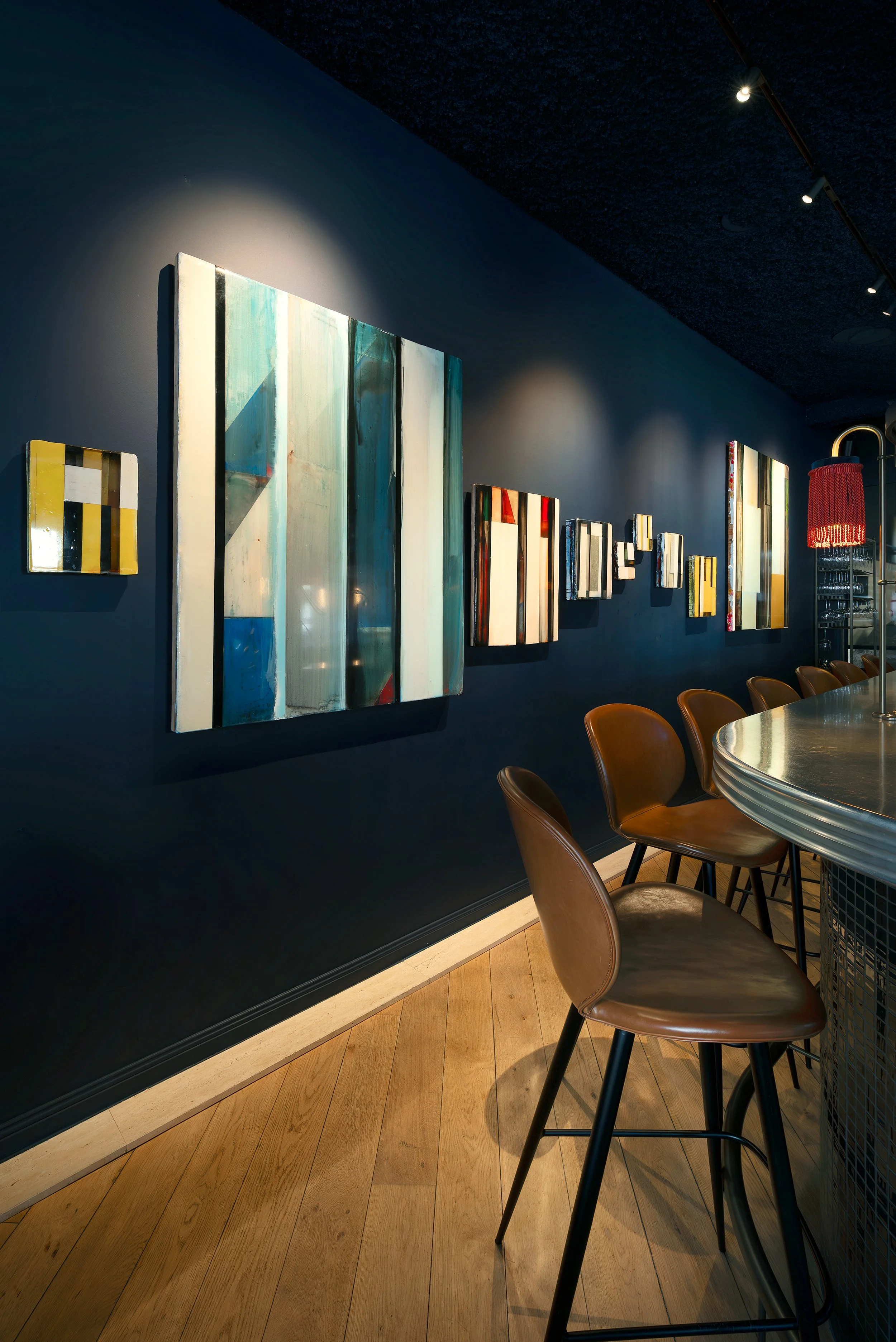 MANOS Build & Maintenance MUST restaurant working site
Art gallery with abstract paintings on a navy blue wall, wooden floor, and bar stools at a curved bar counter.