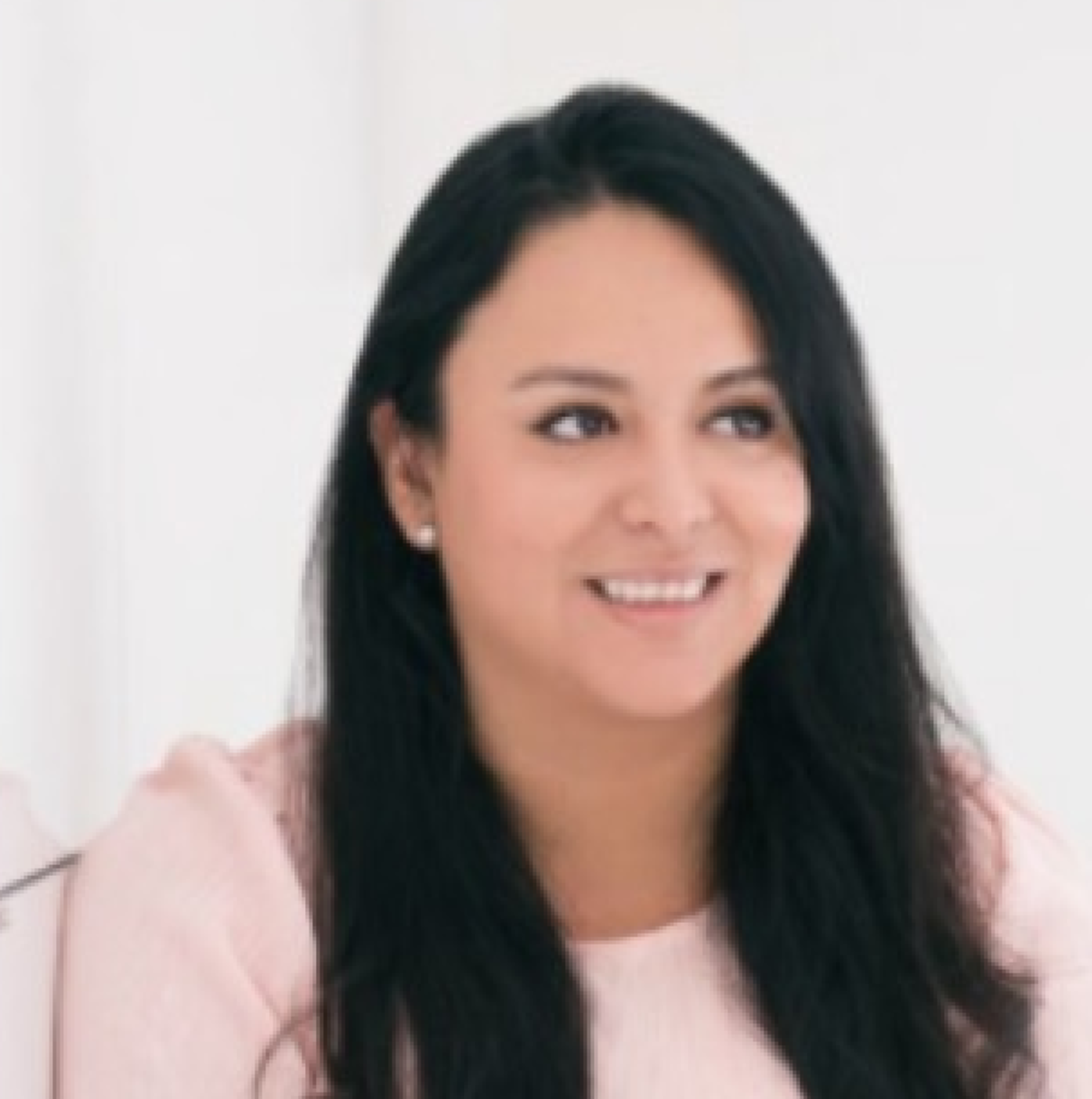 A woman with long black hair wearing a pink top, smiling, against a plain white background.
