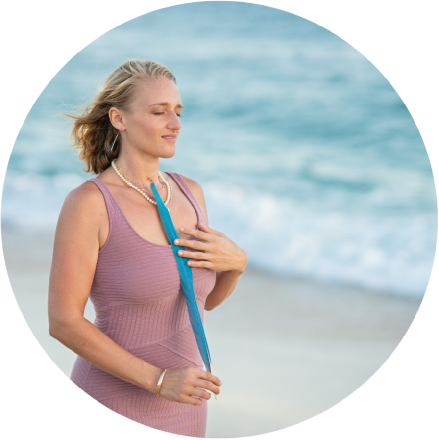 The Embodiment Doula, Rachael Lanehart on the beach on Maui, holding a blue feather near her chest with her eyes closed.