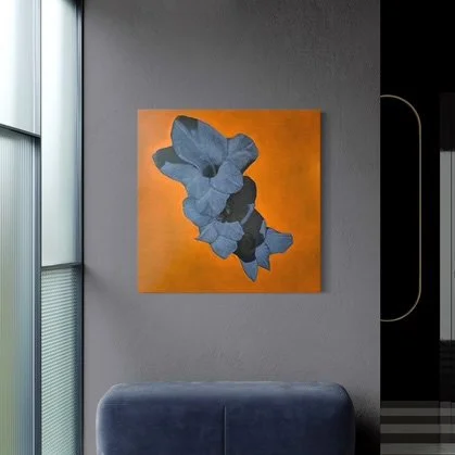 Abstract blue floral painting on a bright orange square canvas hung on a gray wall, next to a large window.