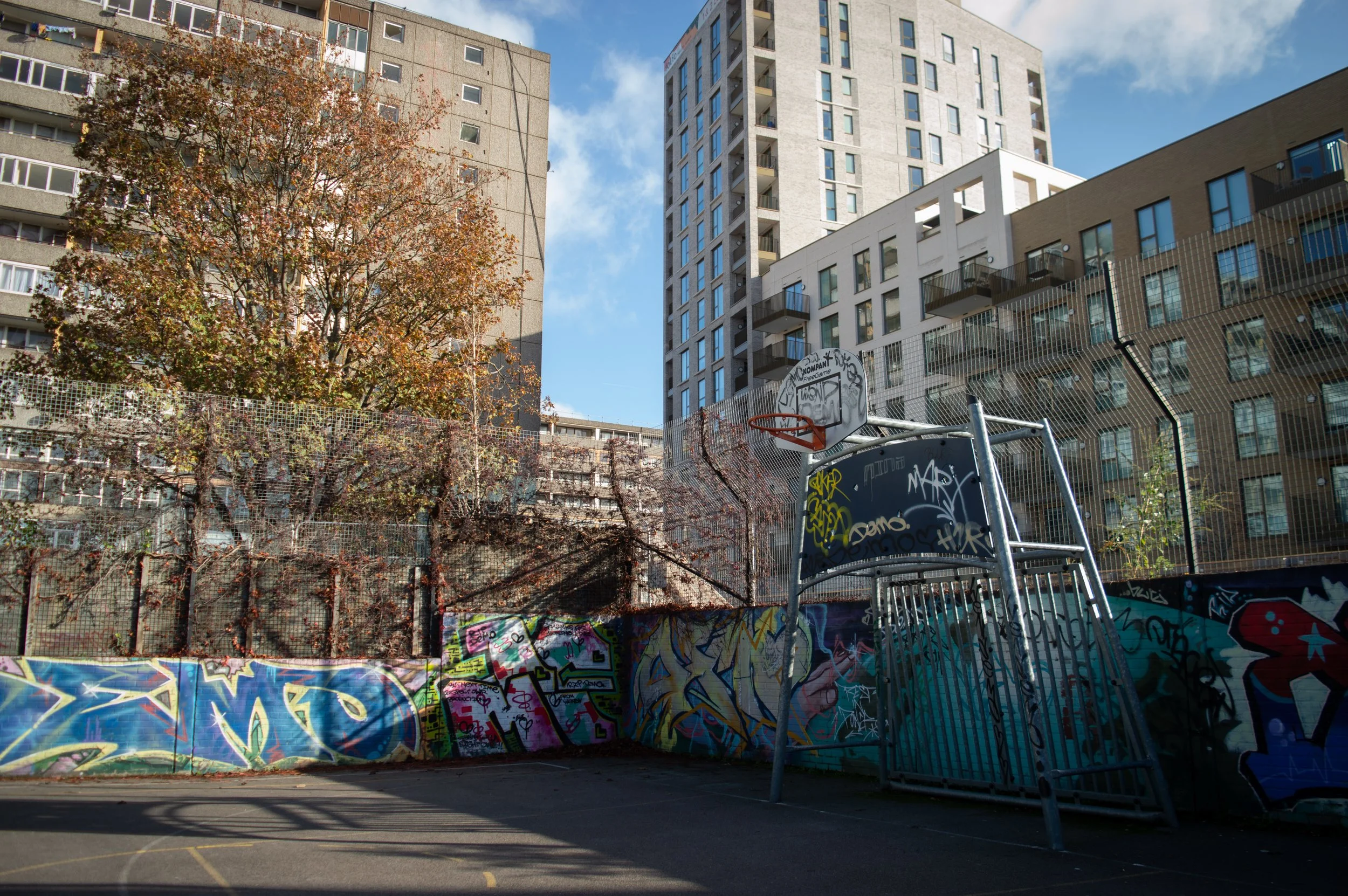 basketball court with graffiti all over it with Aylesbury Estate in the background on the lefthand side and on the righthand side is the new estate which was once part of Aylesbury