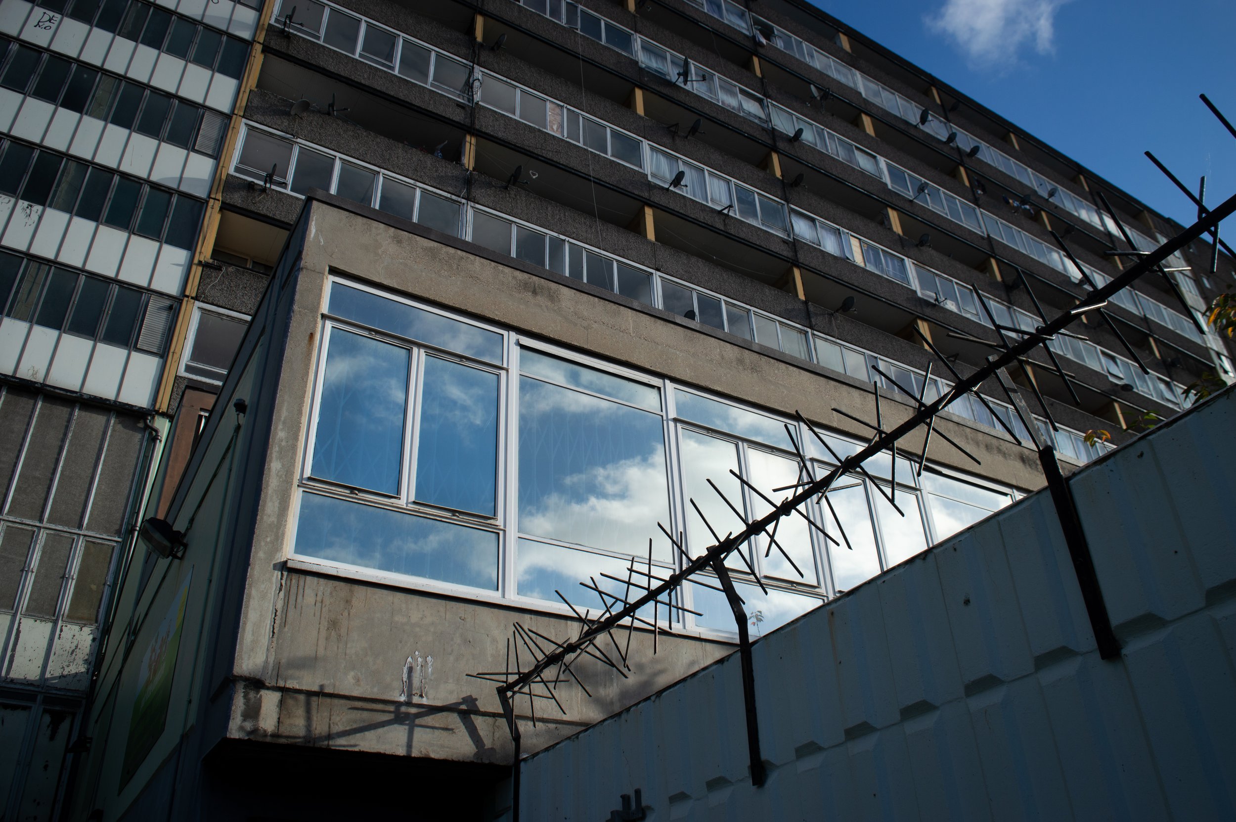 large window at Aylesbury estate with the sky showing in the reflection of the window and a construction fence with large barbed wire above it