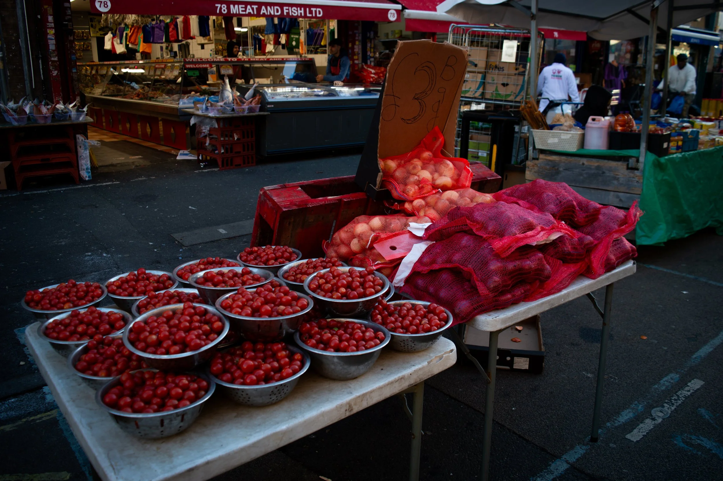 metal bowls of red cherry tomatoes and red bags of white and red onions on a stall at East Street Market 