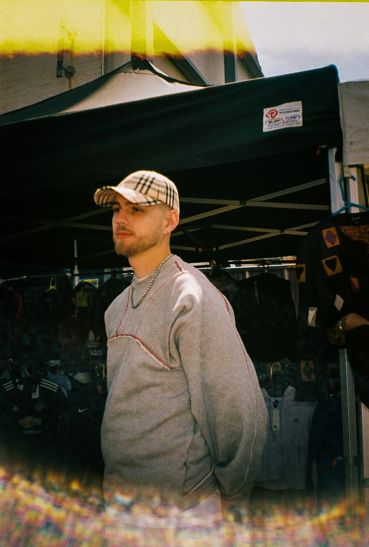 portrait of a young man facing away from the camera at a market in Dudley wearing a tracksuit and Burberry baseball cap 