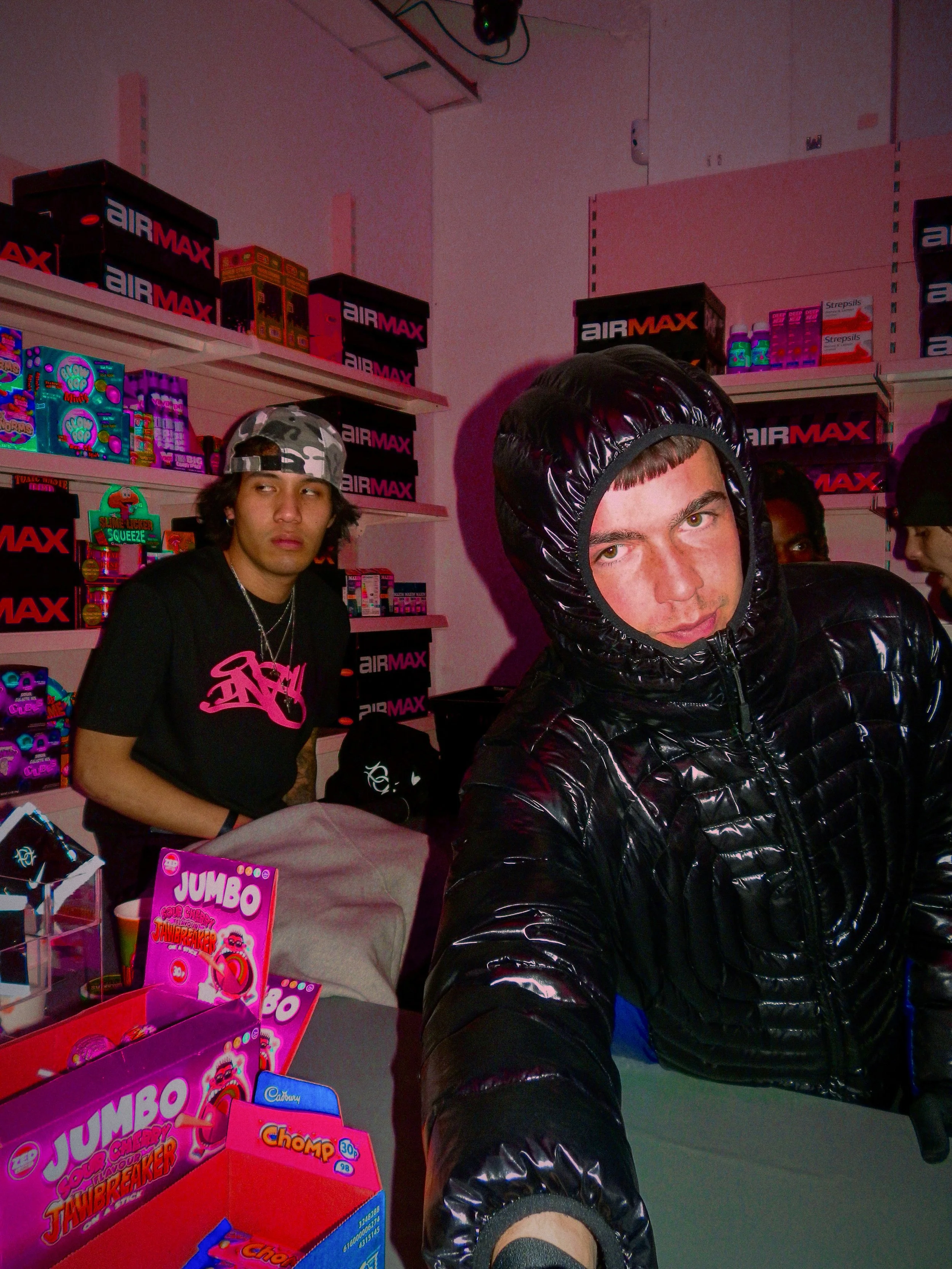 two young men, one of them is sitting in the background looking away from the camera and the other is reaching towards the camera from behind a counter at the nike past down vintage pop up sh