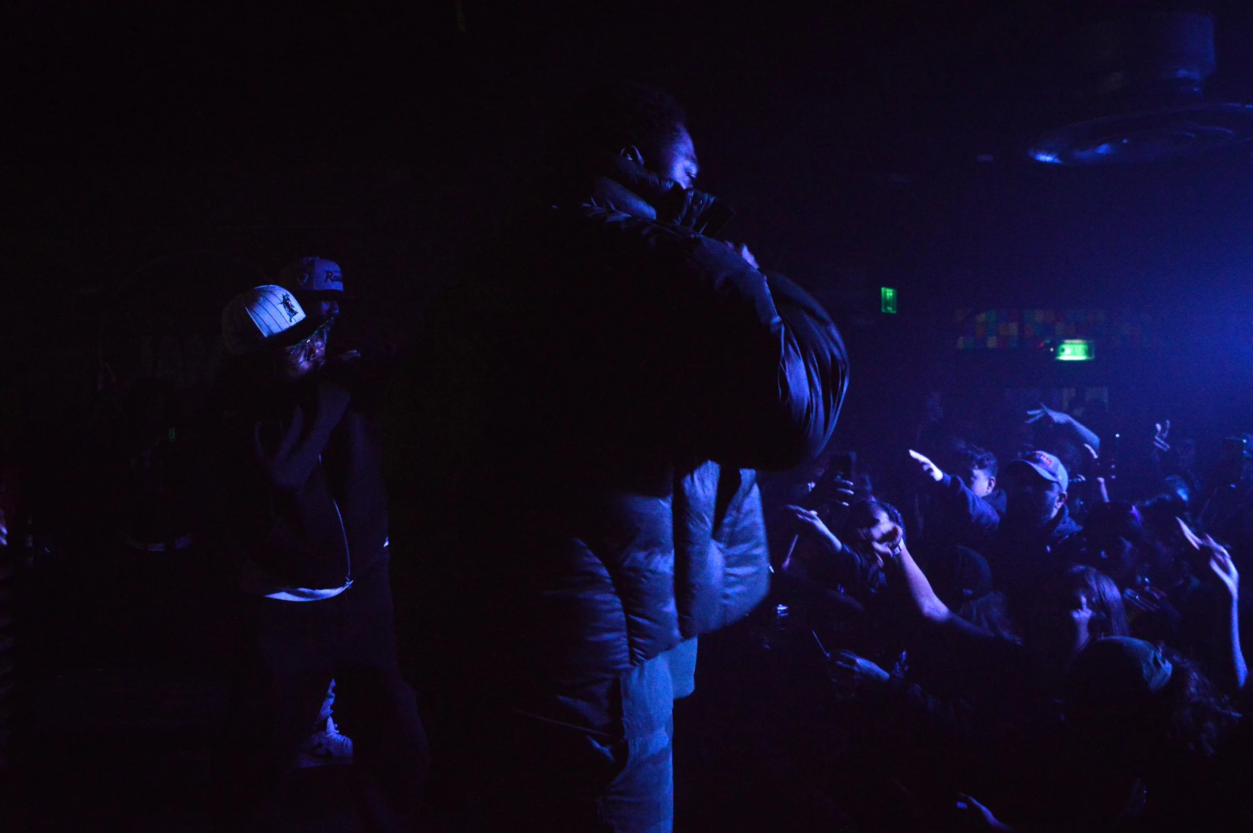 People at a London nightclub dance under blue lighting with some raising their hands, while others take photos or videos.