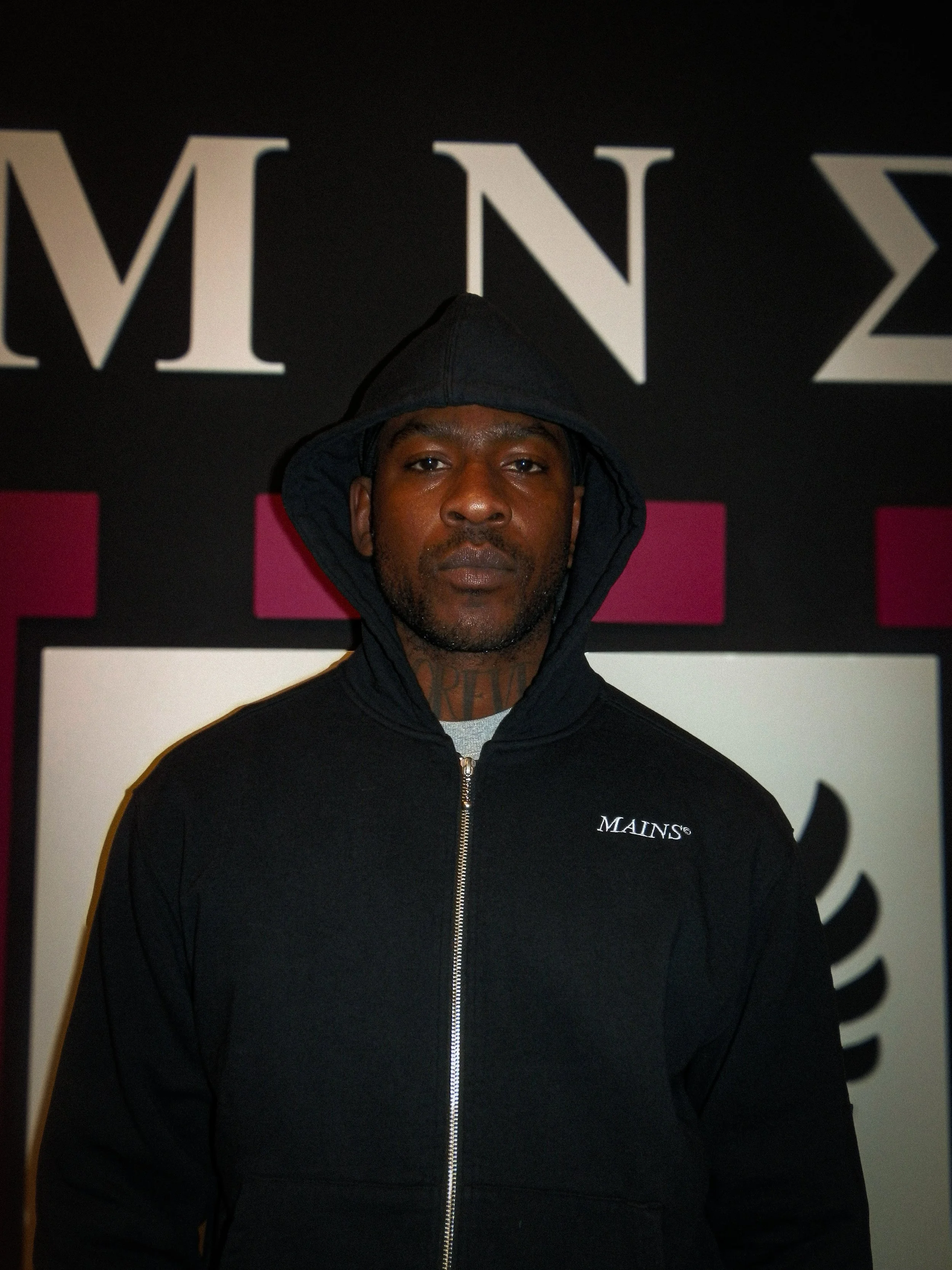Portrait of musician Skepta at his Mains clothing brand pop up store with aa sign of his logo behind him