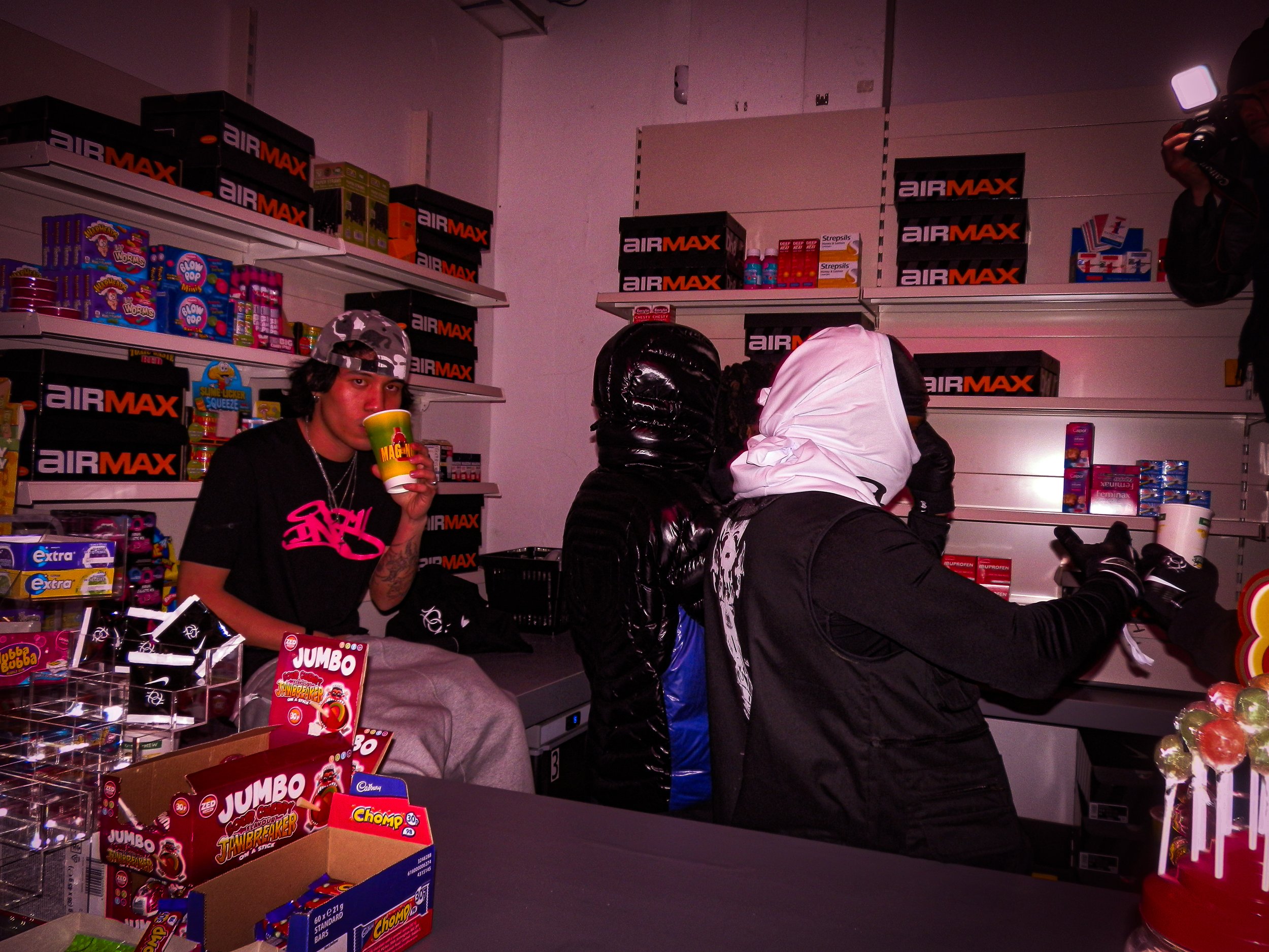 three young men working behind the counter at the Pastdown Vintage x nike pop up shop, one on the left sat on a surface and two stood with their backs facing the camera