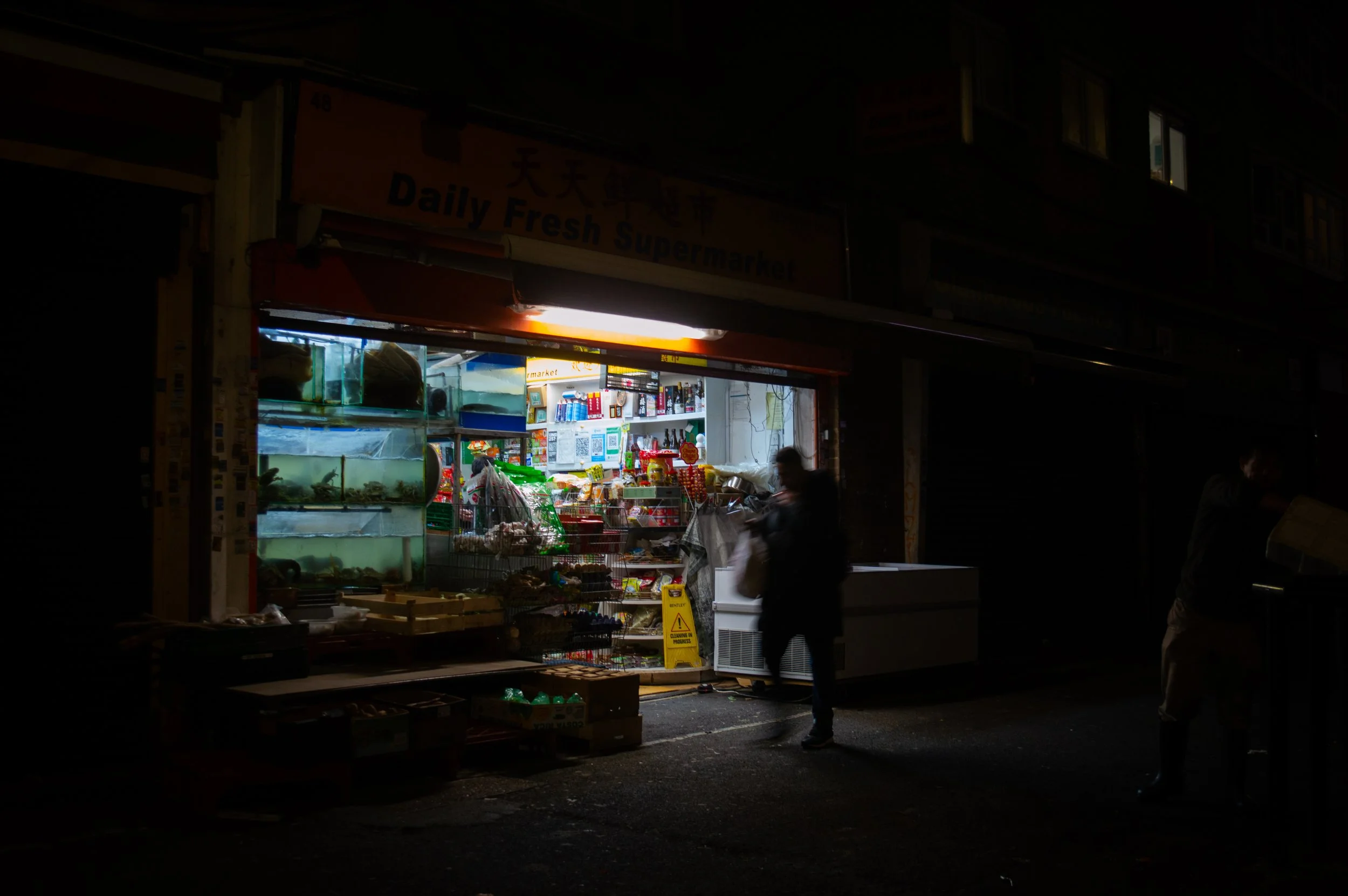 evening landscape of the outside of an indoor market style ethnic food shop with aa customer walking past
