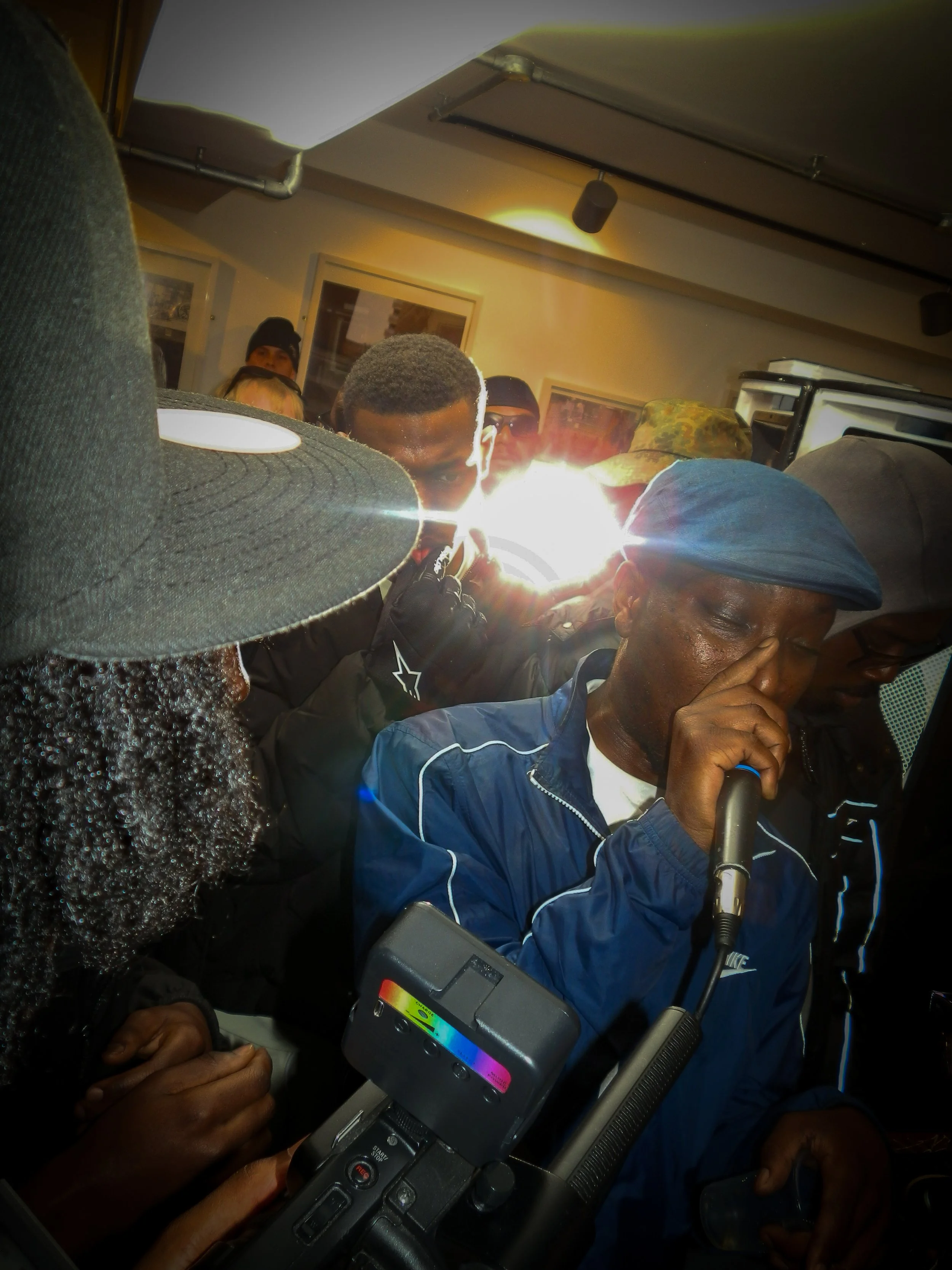 mc bruza performing into a mic and cam corder at victory lap pop up cypher for simon wheatley don't call me urban book launch