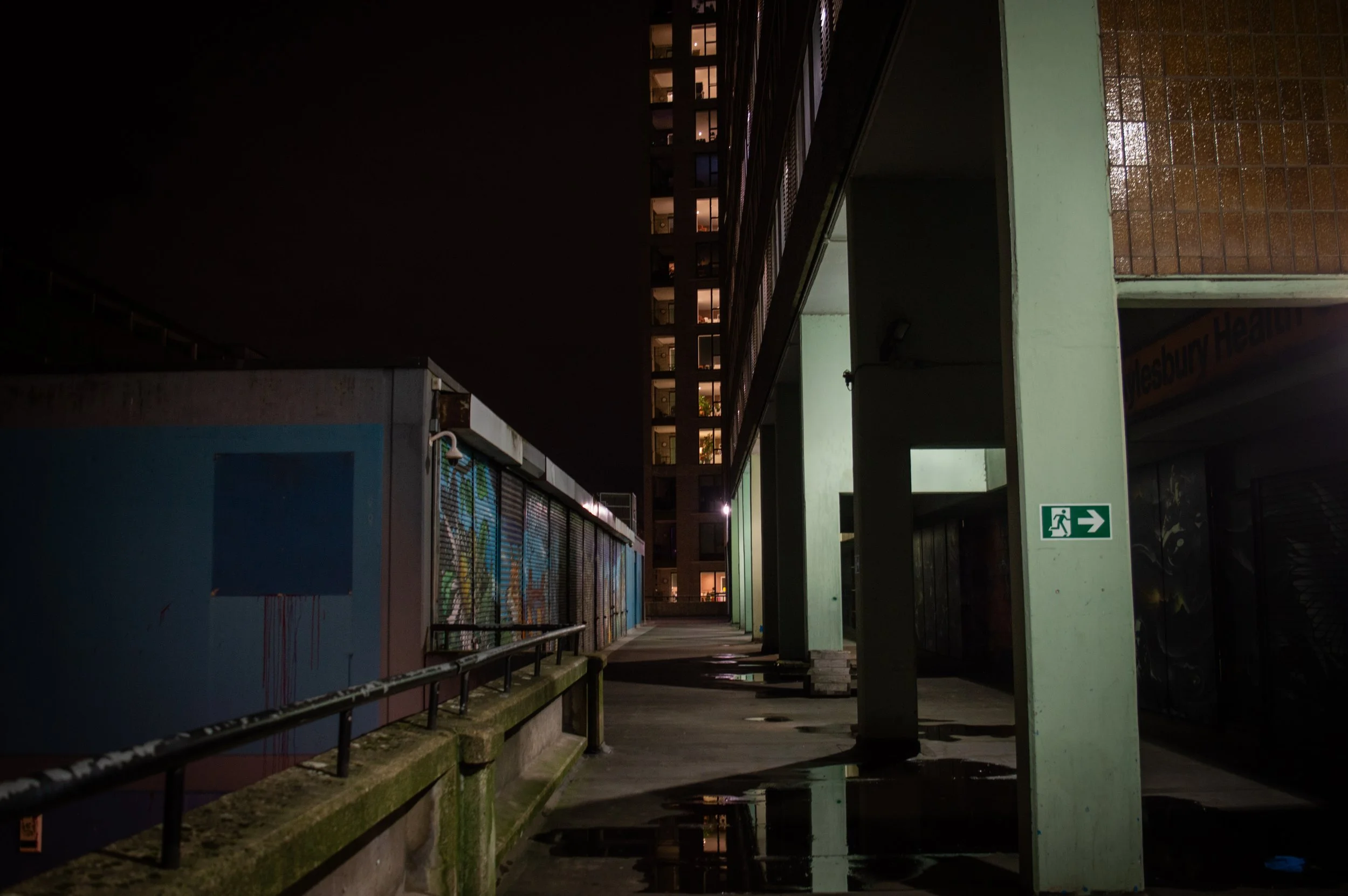 the top floor of a rundown council estate tower block with graffiti facing the new build estate across from it