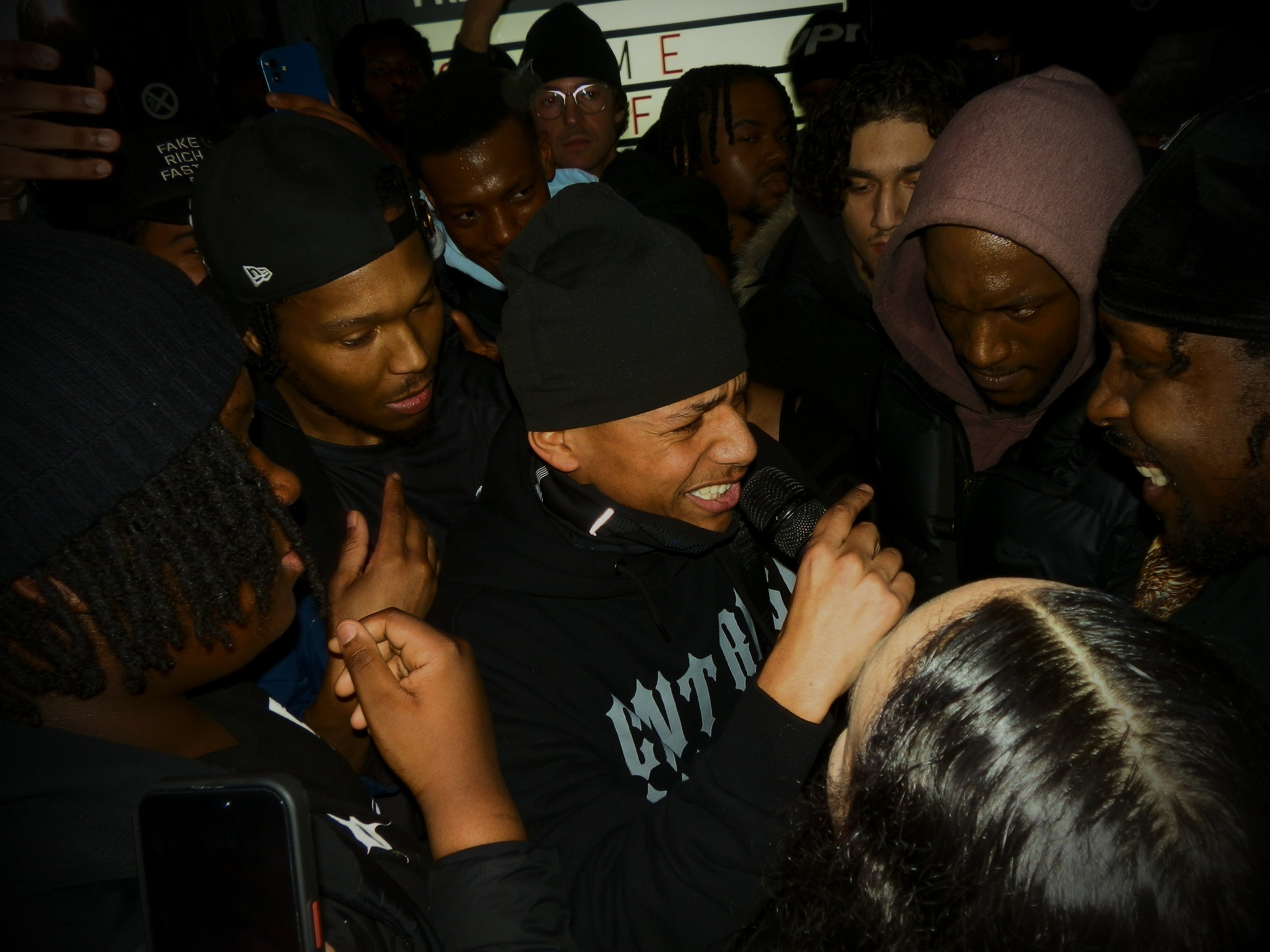 A member of the crowd spitting on the mic at jme grime mc fm pop up in box park Shoreditch with the crowd and grime mcs surrounding him 