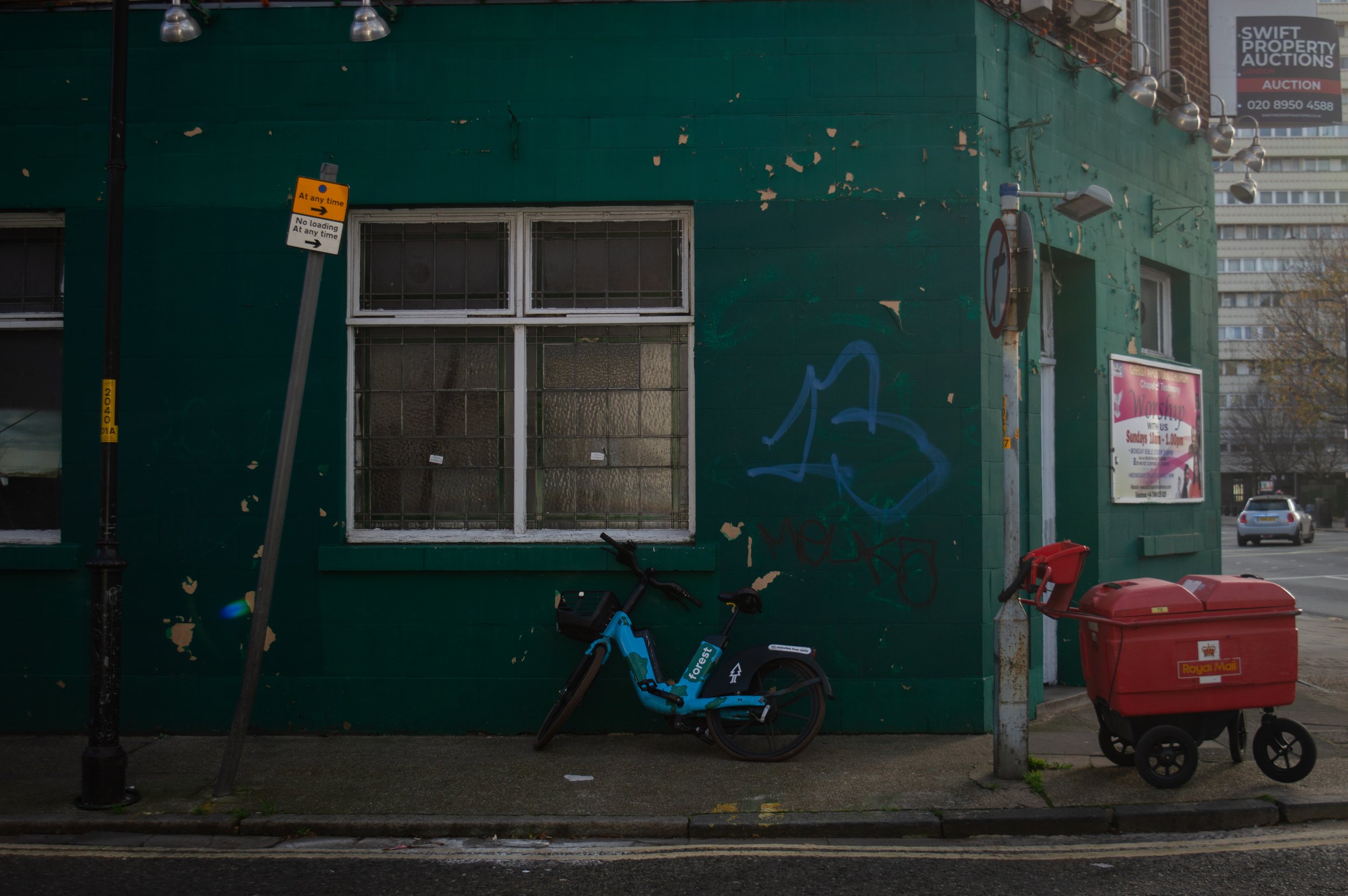 a pushbike up against a wall and a Royal Mail trolley outside of a rundown building for sale 
