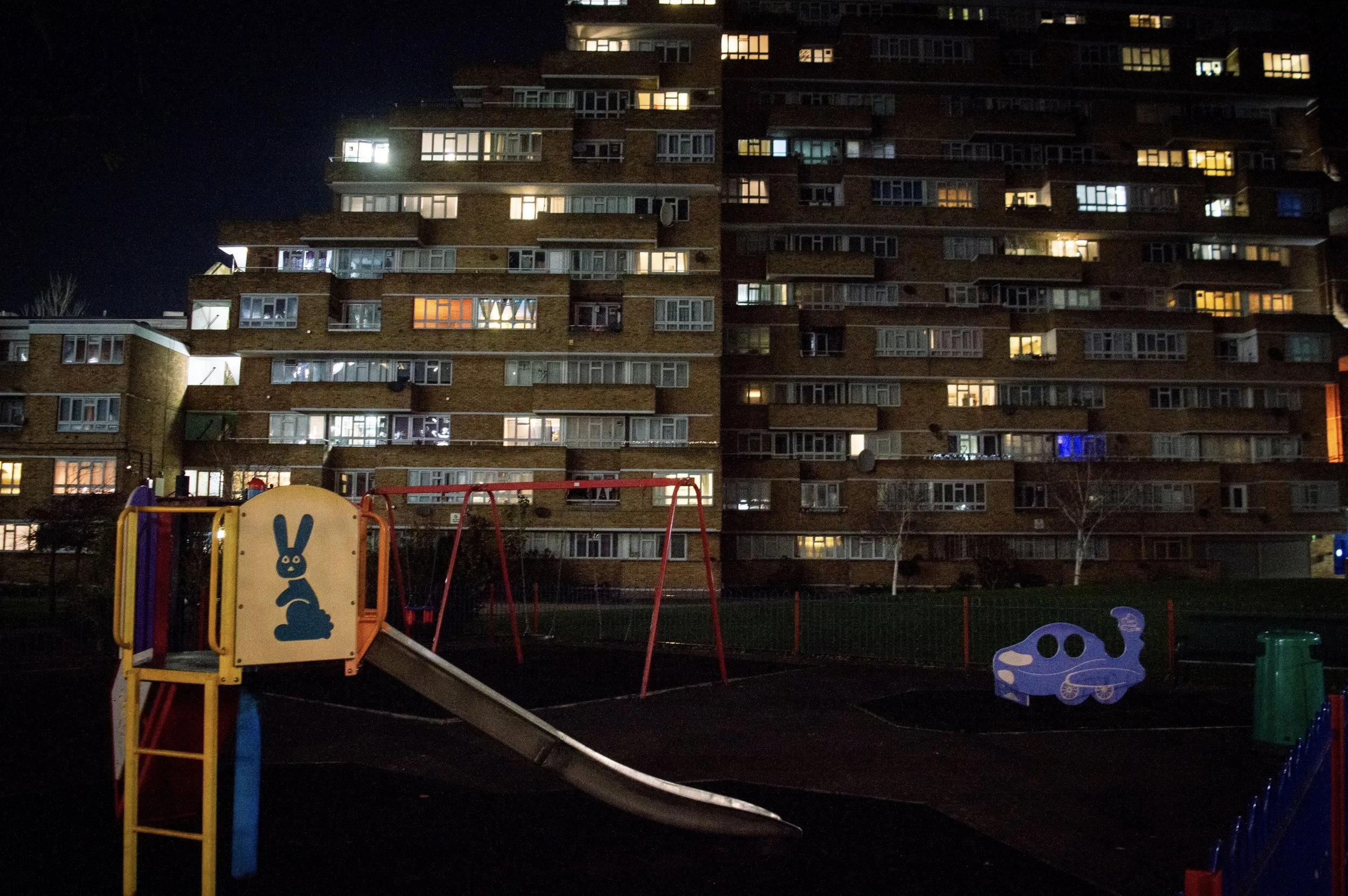Dawson Heights estate at night with bright lights coming from the windows in the background and a children's park in the foreground