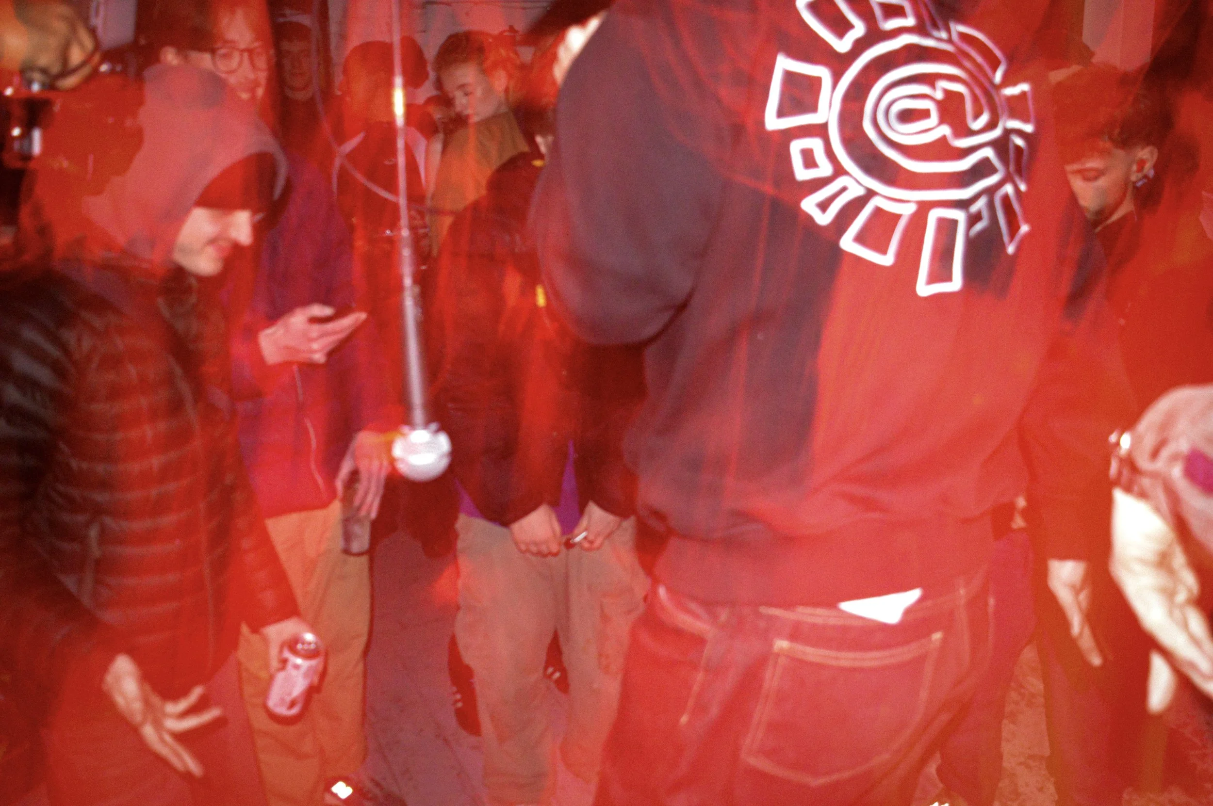 artistic red toned image of a young mans lower half of his body standing in a crowd, microphone next to him , his jumper that has always do what you should do logo on the back of it