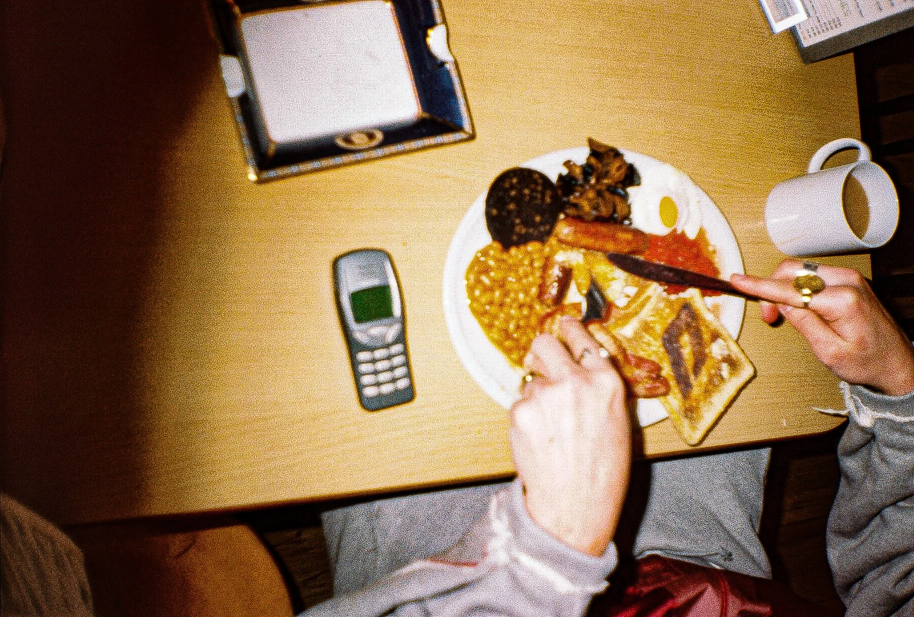 Full English breakfast on a cafe table with a 'D' burnt into toast for the Defenda sportswear logo, surrounding the breakfast is a cup of tea, a nokia phone and a Burberry ashtray 