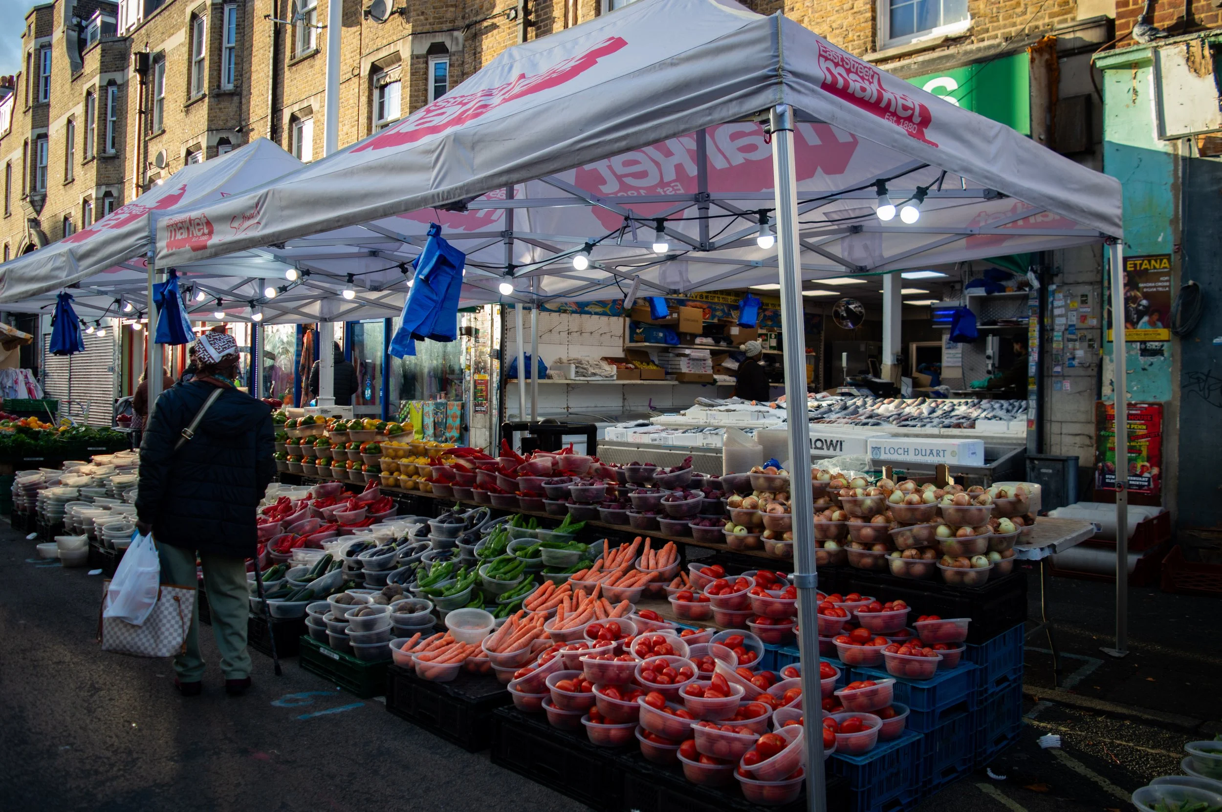 a fruit and vegetable stall with a customer browsing at East Street Market