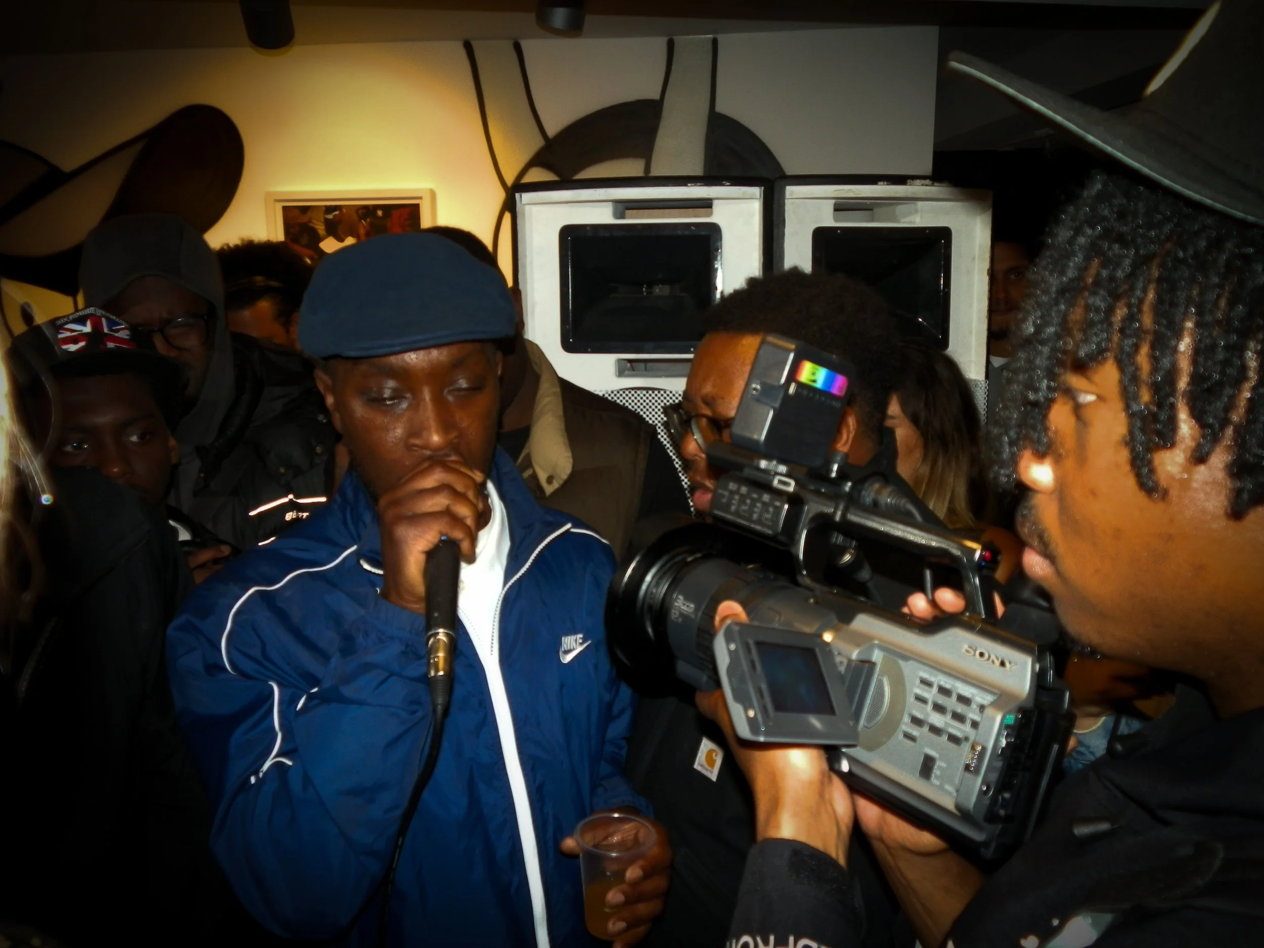 mc bruza performing into a mic and cam corder at victory lap pop up cypher for simon wheatley don't call me urban book launch