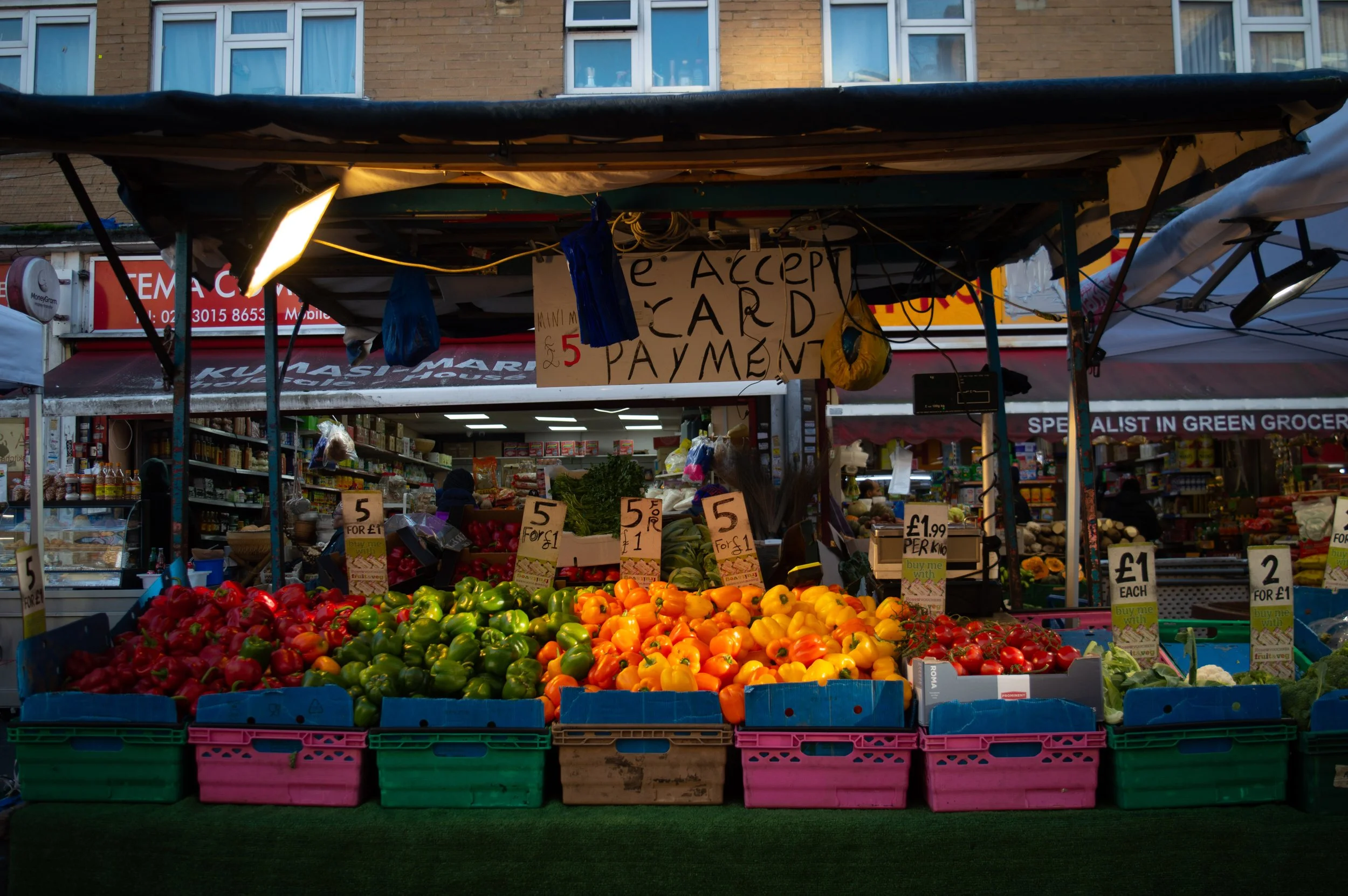 landscape of a fresh produce market stall at East Street Market with a view into the ethnic grocery shop behind 
