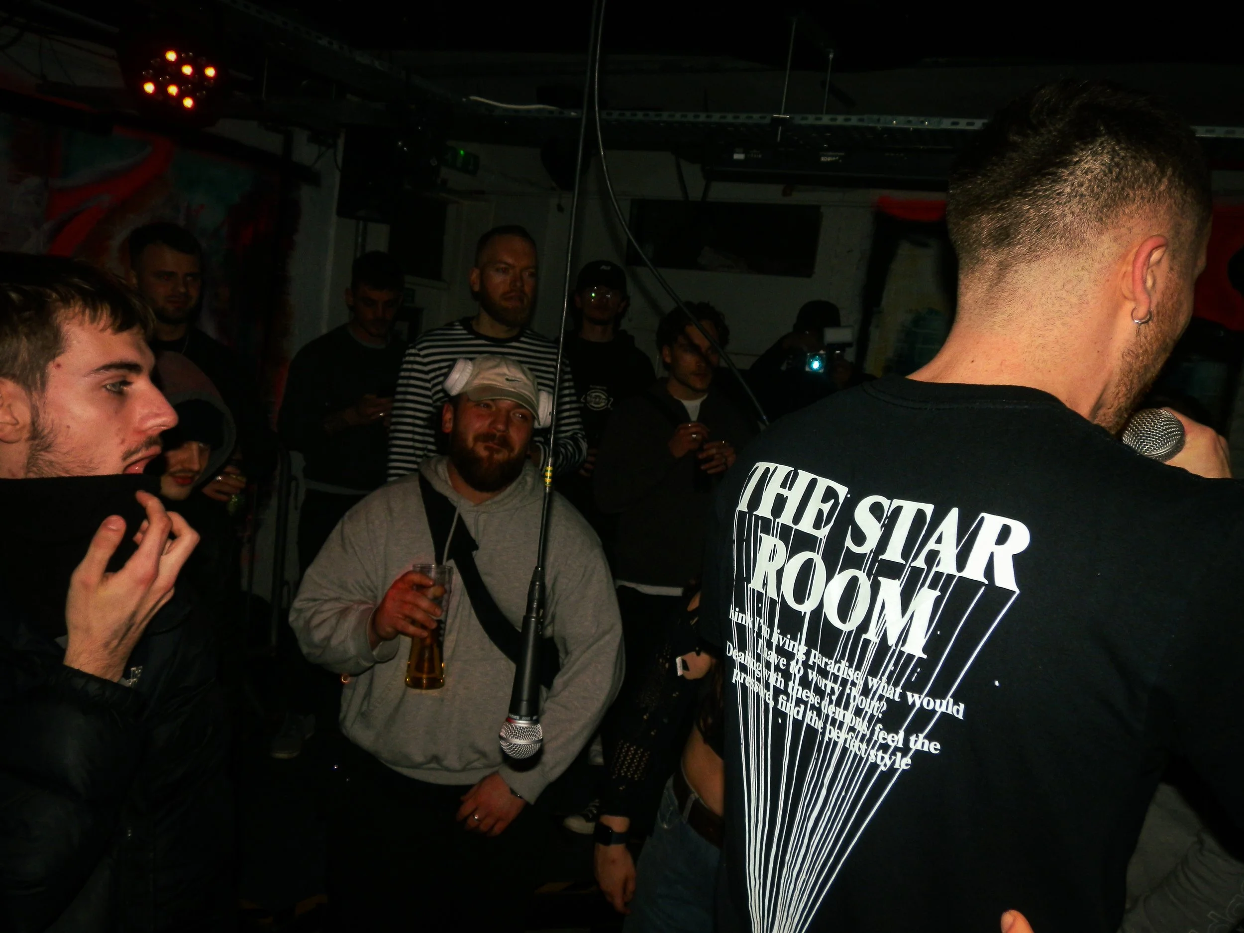 the back of a male mc performing into a crowd with a mic hanging from the ceiling at wheel up grime rave 