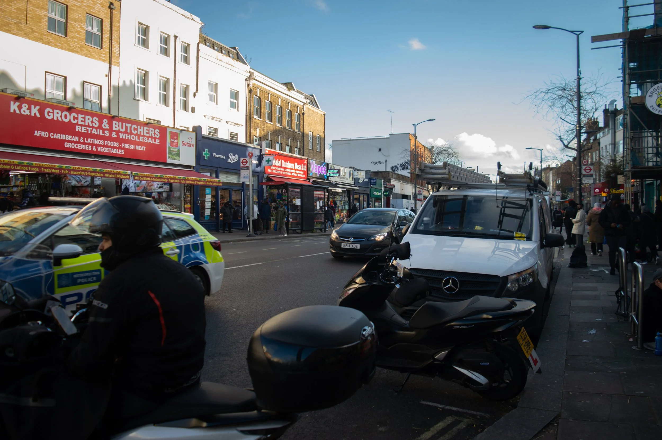 highstreet on Walworth road showing a police car, storefronts and a man on his motorbike 