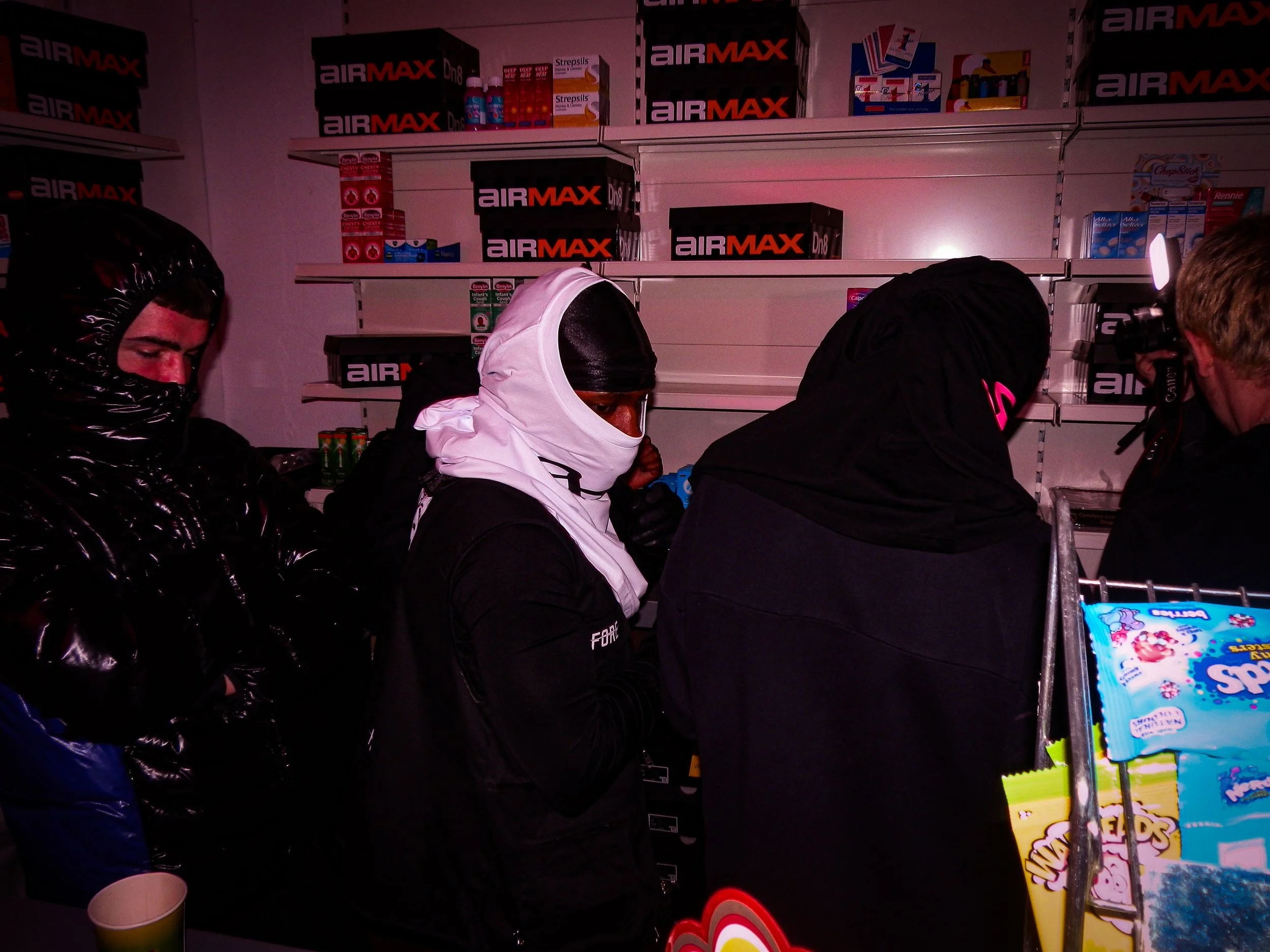 three young men working behind the counter at the Pastdown Vintage x nike pop up shop all covering their faces turning round with their faces covered and backs towards the camera