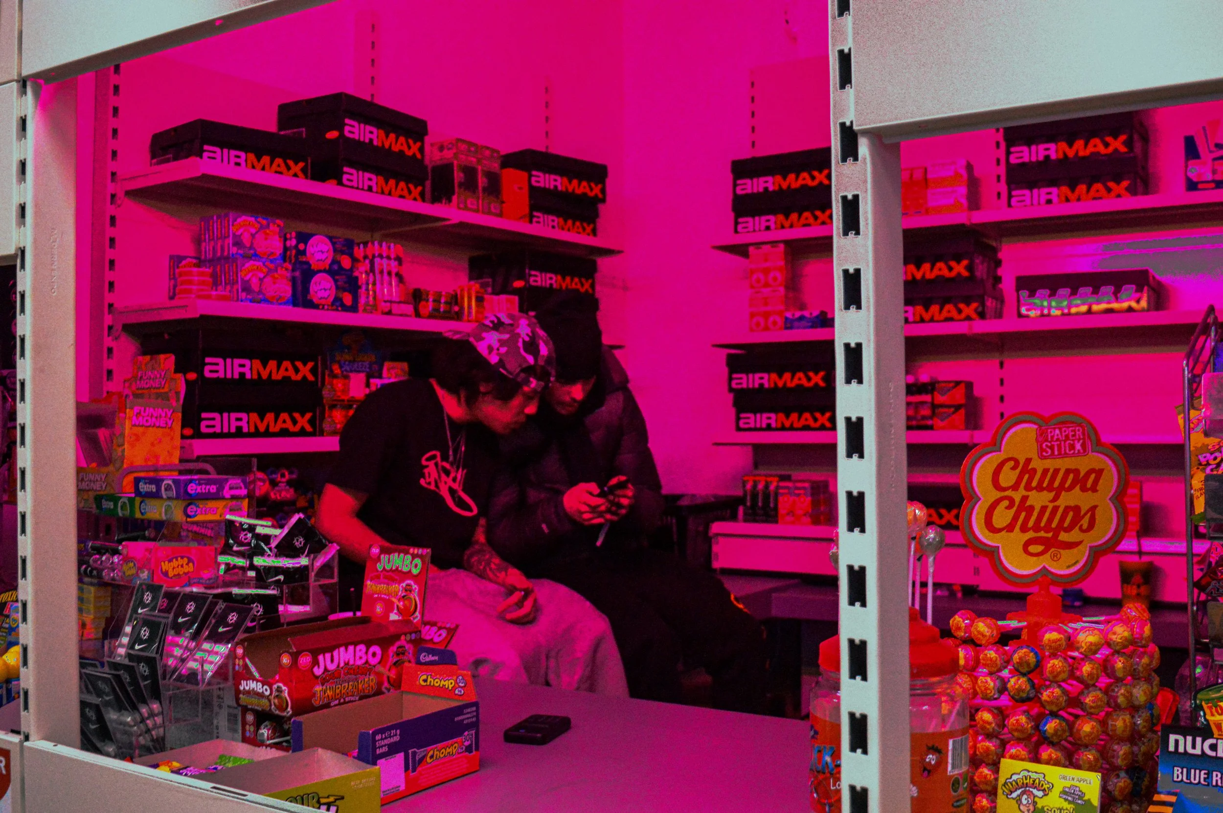 two male staff members sitting on a surface behind the counter under pink lighting 