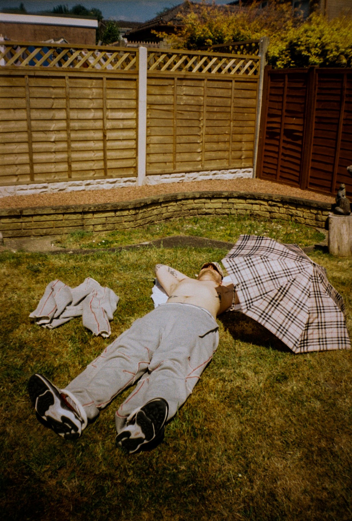 fashion model sun bathing in Defenda sportswear tracksuit, Burberry hat and Burberry umbrella