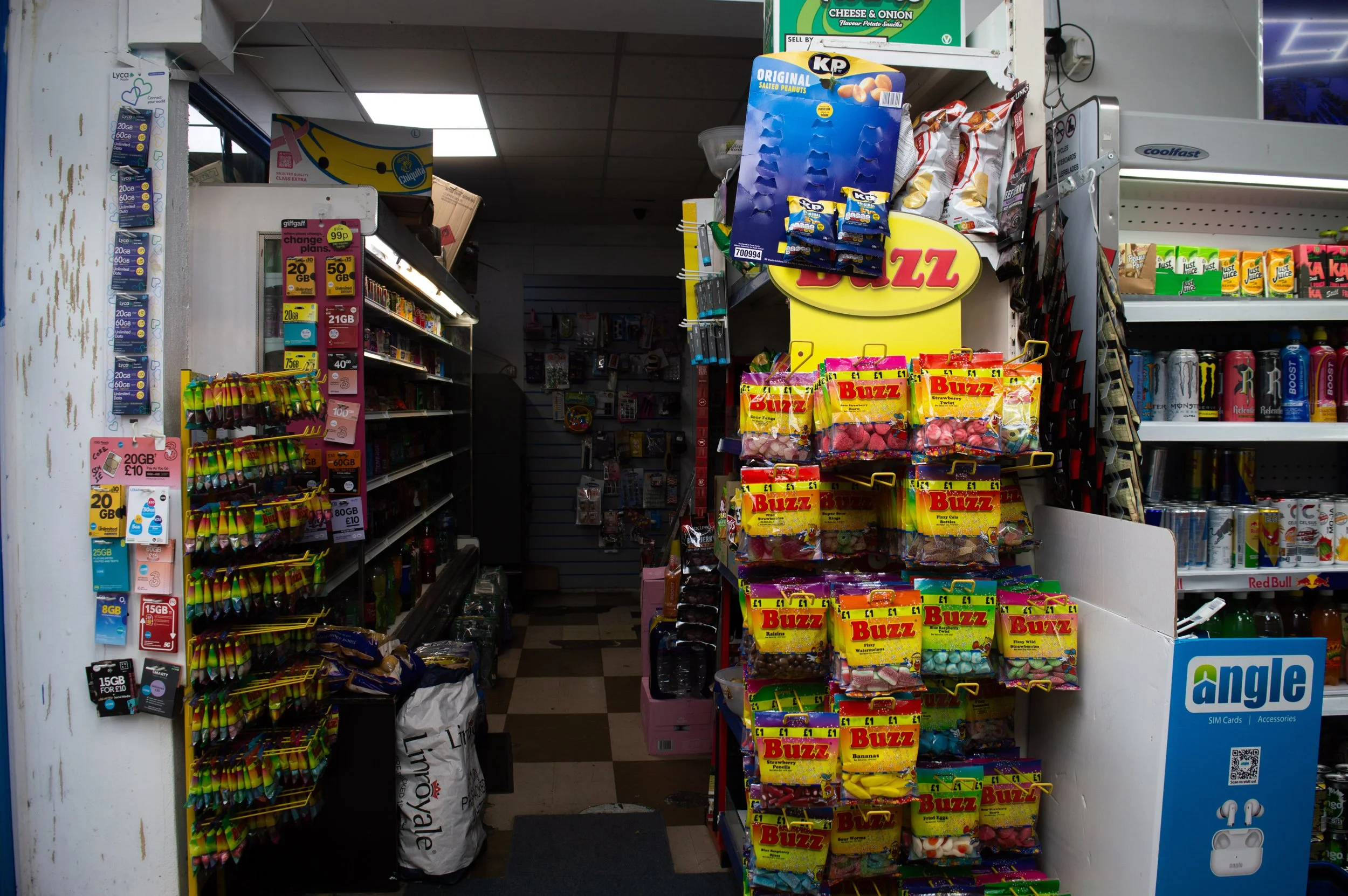 rundown Aylesbury Estate corner shop with bright coloured packaging in the foreground and dark lights coming from the backroom 