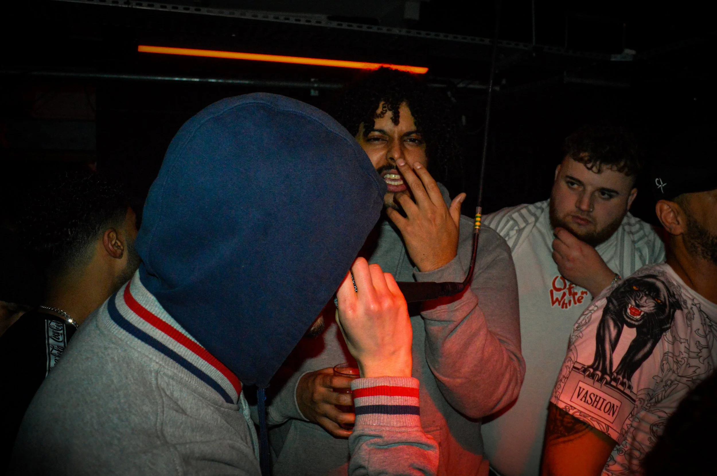 the side of an mc performing into a mic with other energetic musicians and crowd behind him