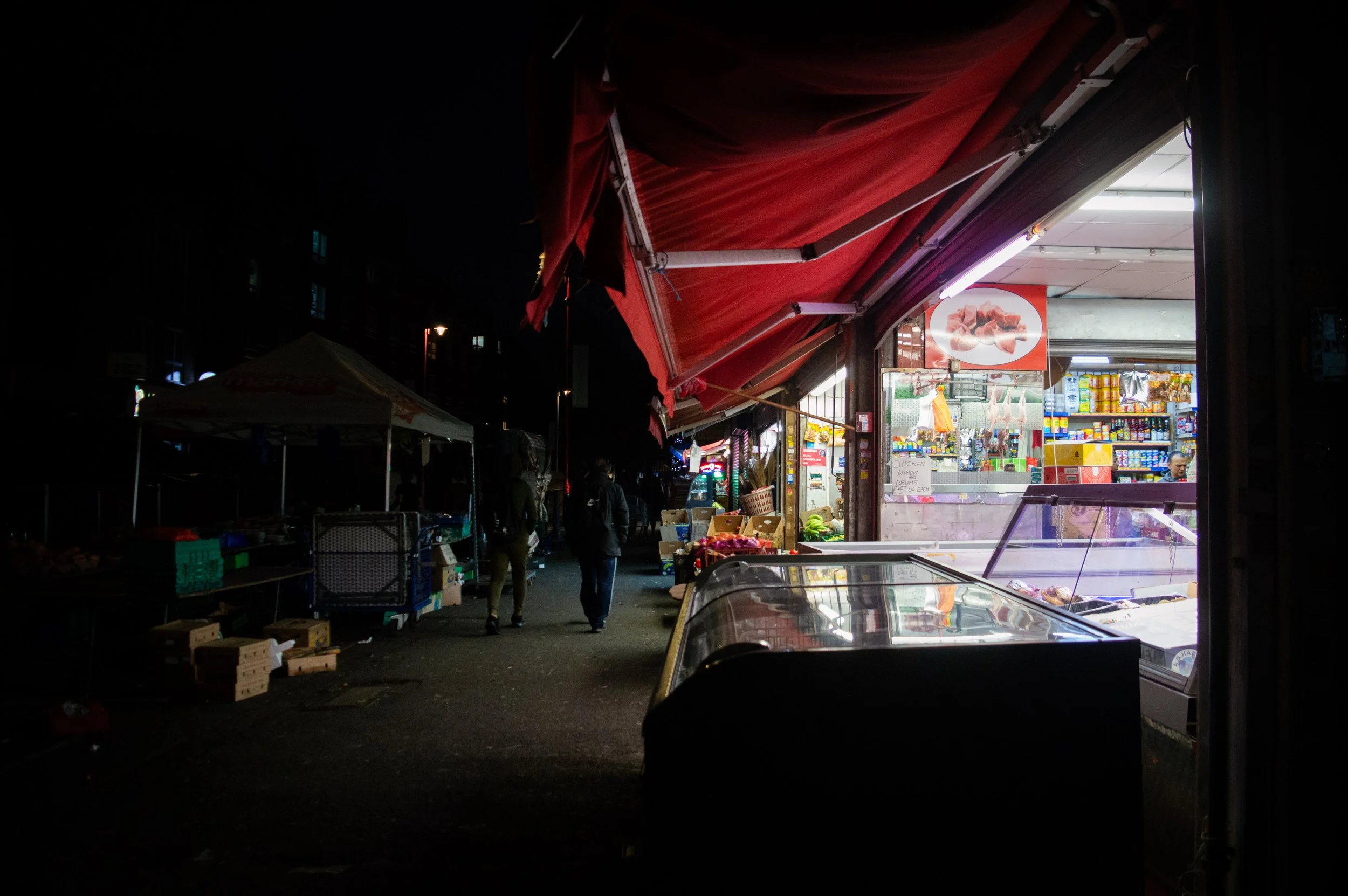 evening landscape of the outside of an indoor market style ethnic food shop with a view of people walking along a path