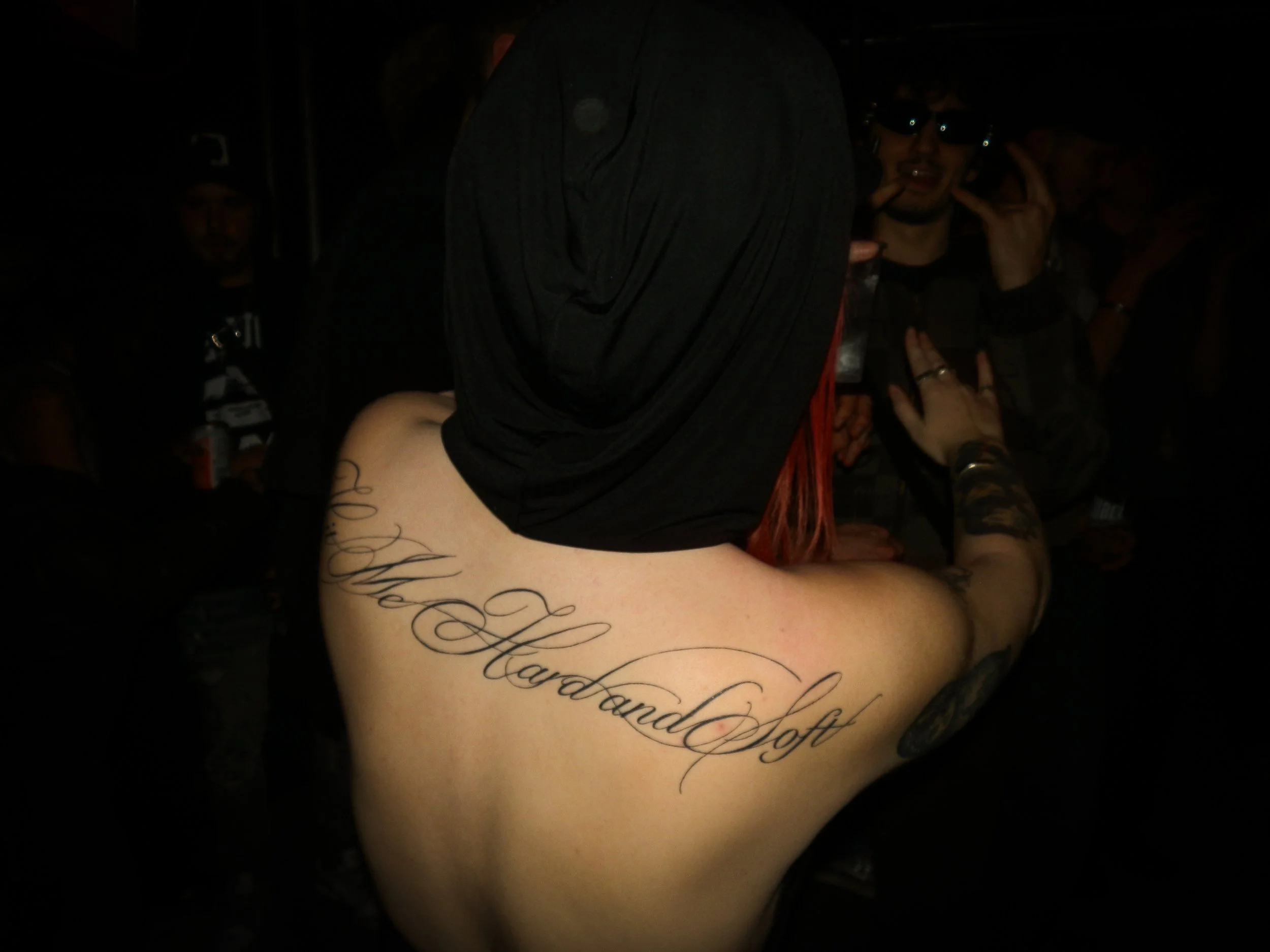 the back of a woman dancing in a rave with an open back top showing large cursive tattoo across her shoulders