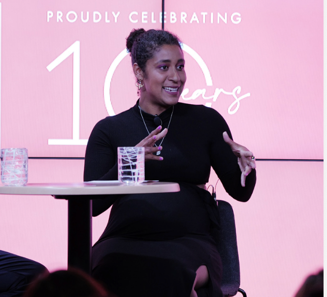 A modern white house nestled among dense green trees and shrubs on a hillside, with solar panels on nearby structures in the background.