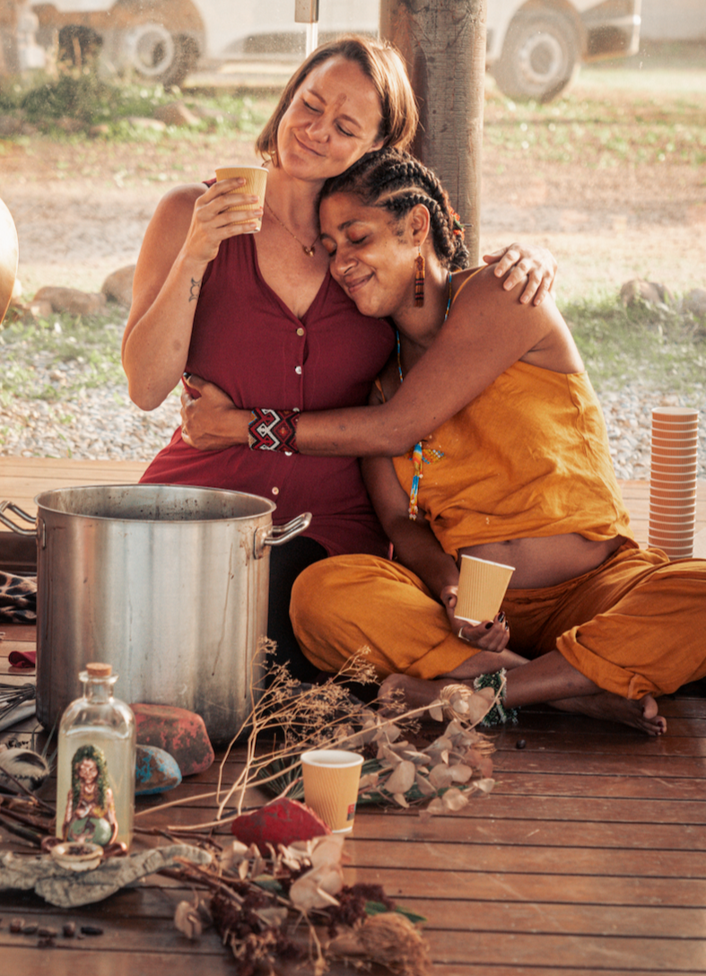 A modern white house nestled among dense green trees and shrubs on a hillside, with solar panels on nearby structures in the background.