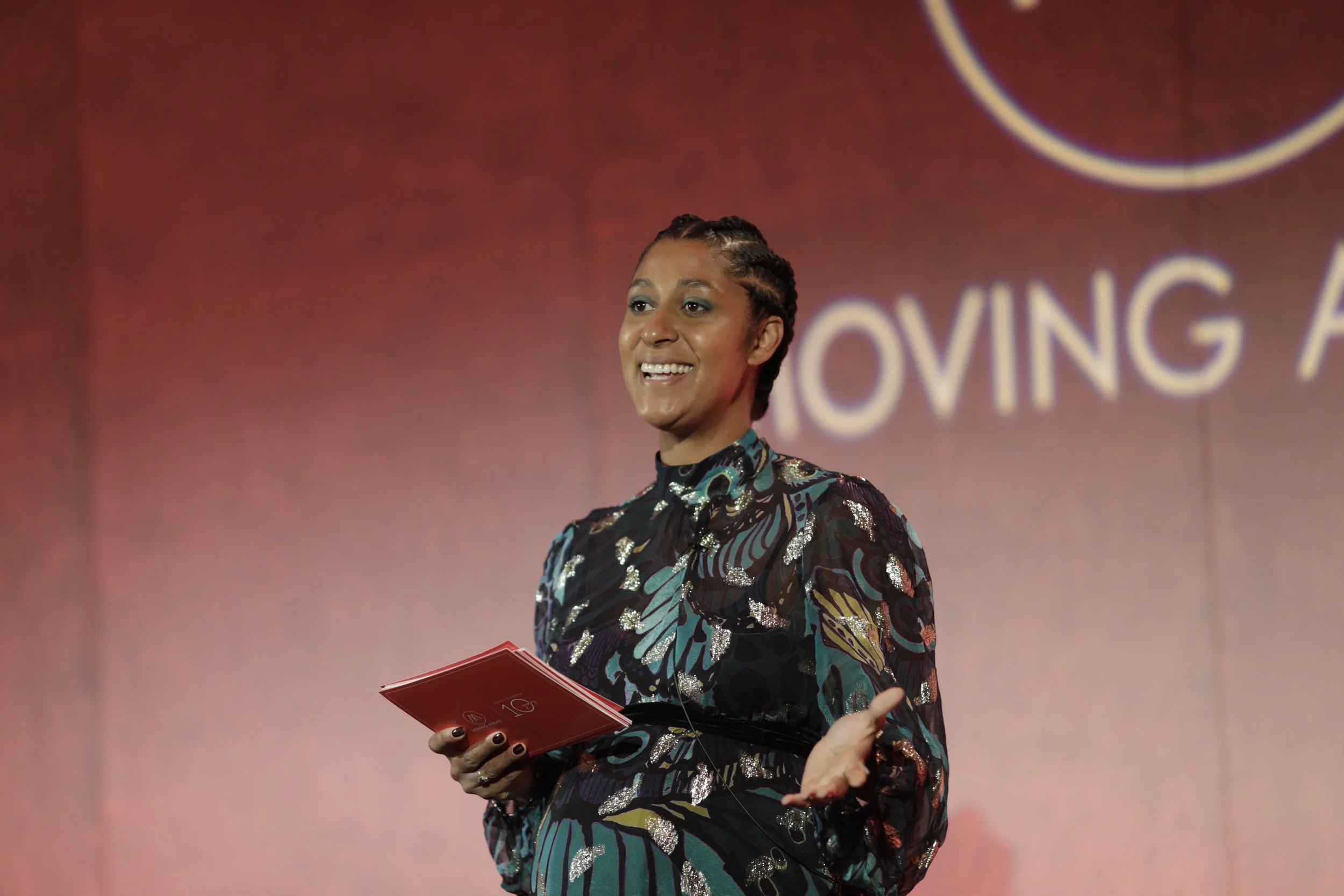 Holiday Phillips wearing headphones mixing music at a pink-themed venue with wall art, a window, and various equipment around her.