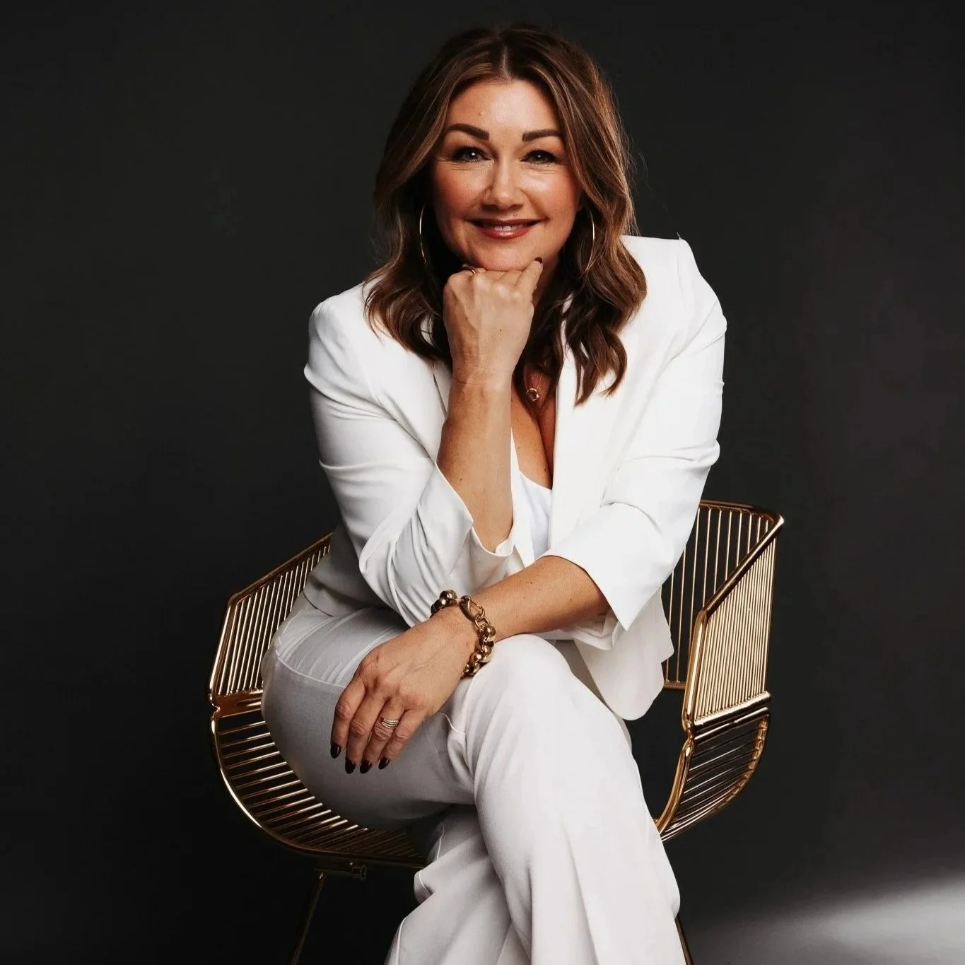 Sarah Schneeweis seated in a white suit against a dark background